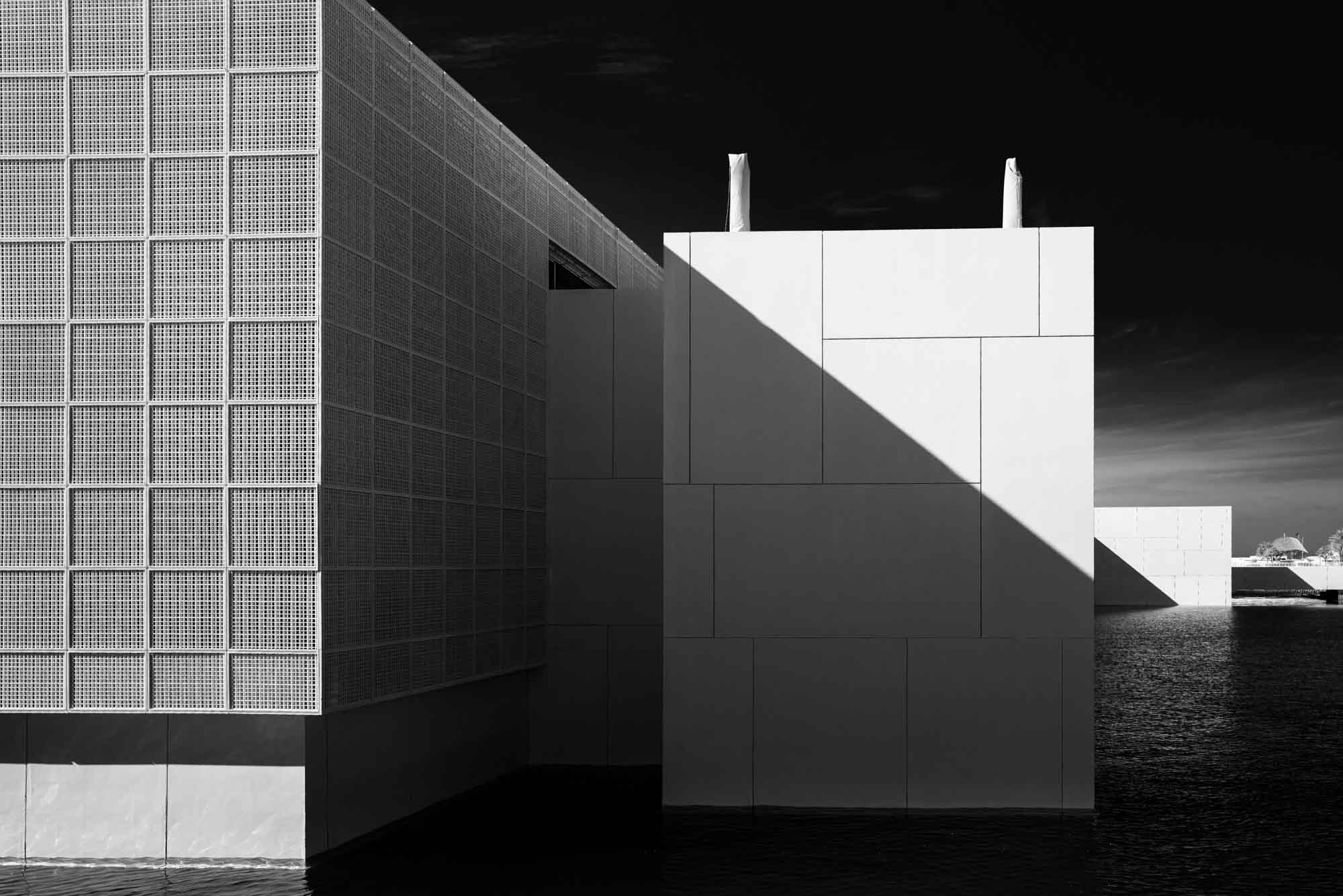Modern architecture with geometric patterns and light contrasts over water. Black and white.