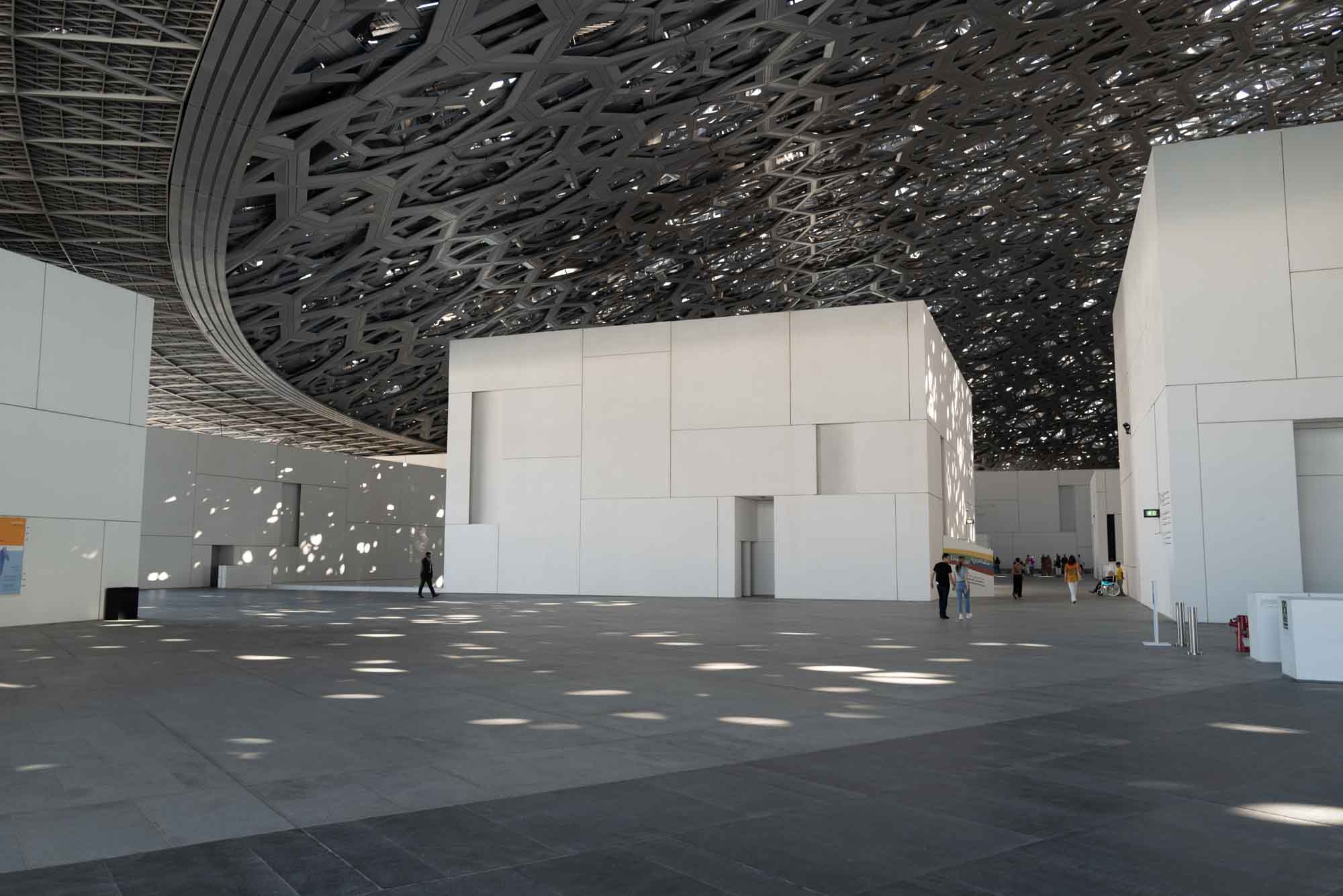 Modern architectural interior with intricate ceiling design and white walls, natural light patterns on the floor.