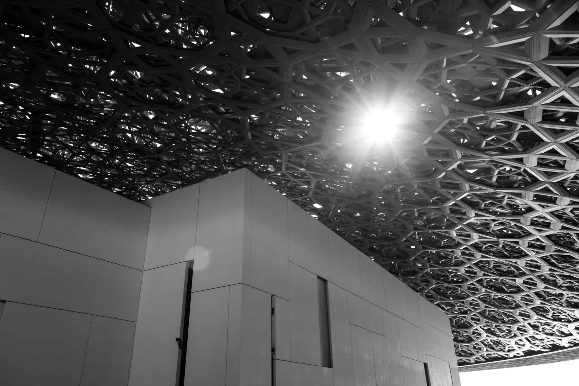 Futuristic architectural ceiling design with sunlight streaming through intricate patterns. Black and white photo.