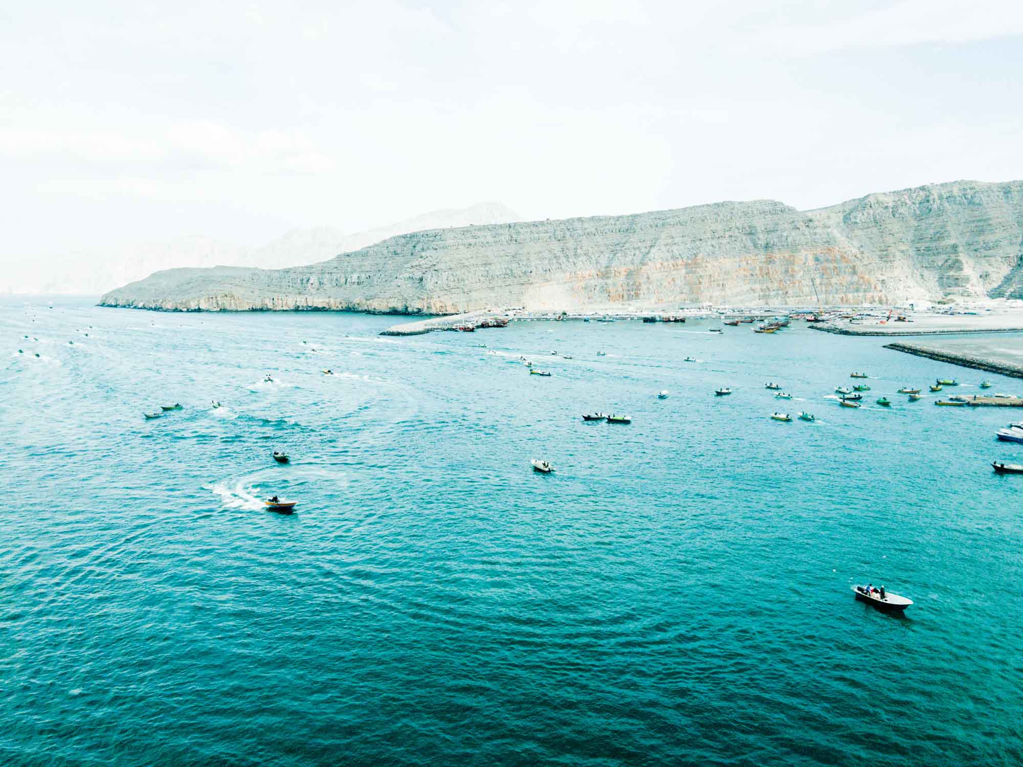 Boats navigate turquoise waters near rocky coastline under a clear sky, creating a scenic maritime landscape.