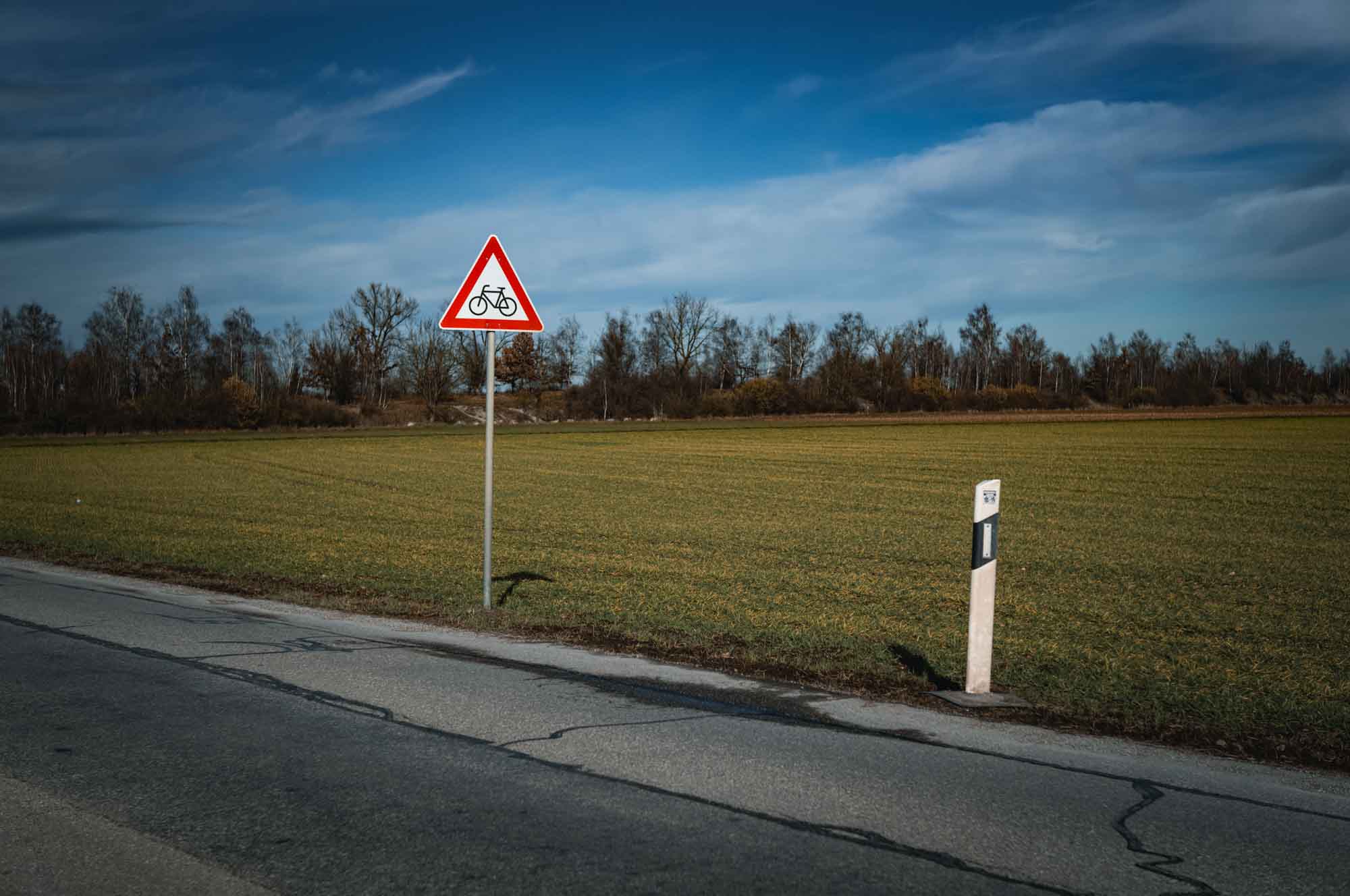 Bicycle warning sign on a rural road beside green fields and blue sky background.