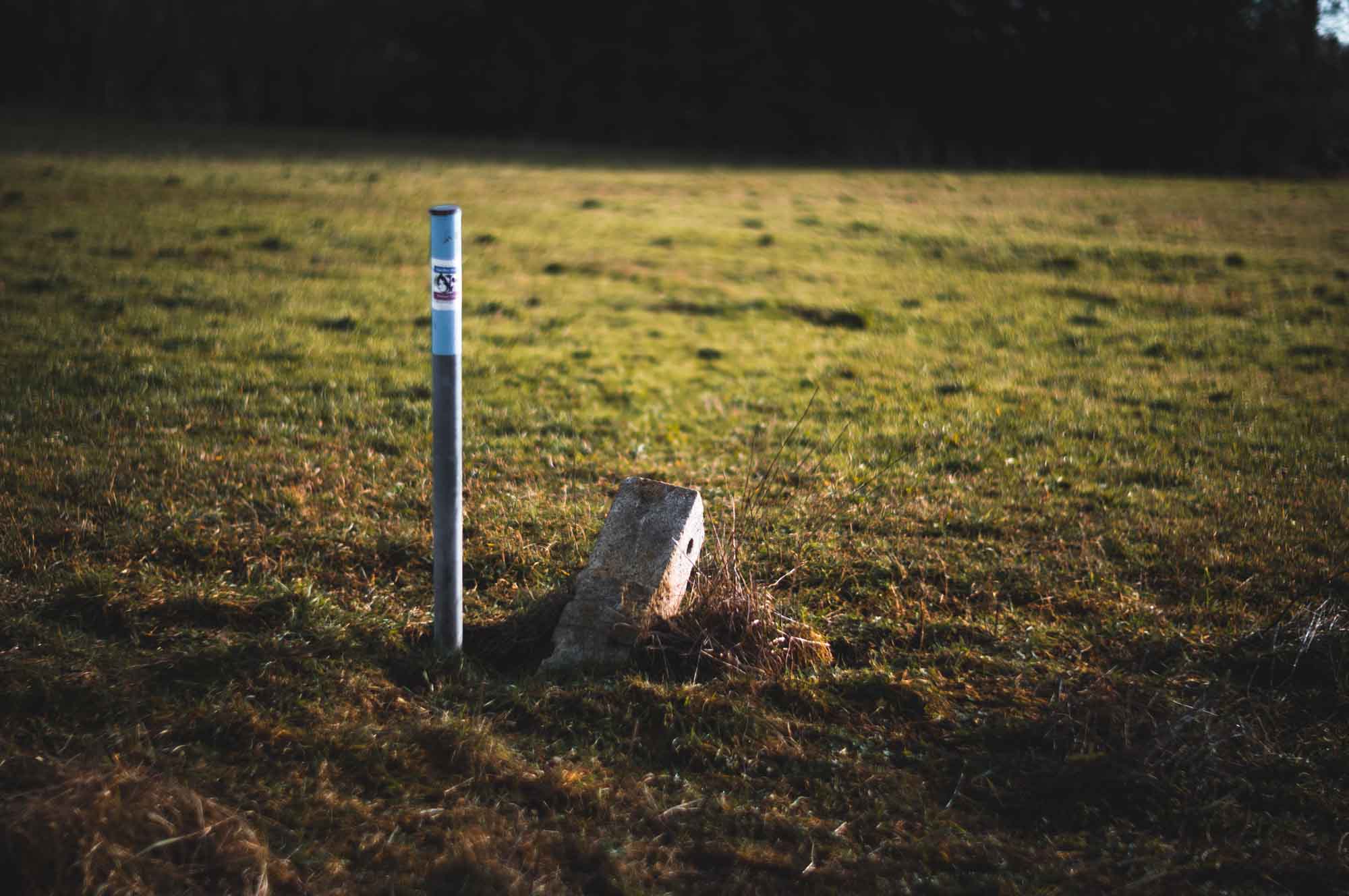 Metal post and concrete block in a grassy field under sunlight.
