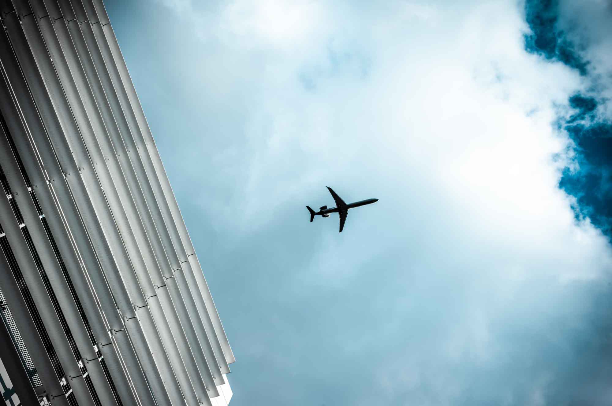 Airplane flying above modern building against blue sky with clouds.