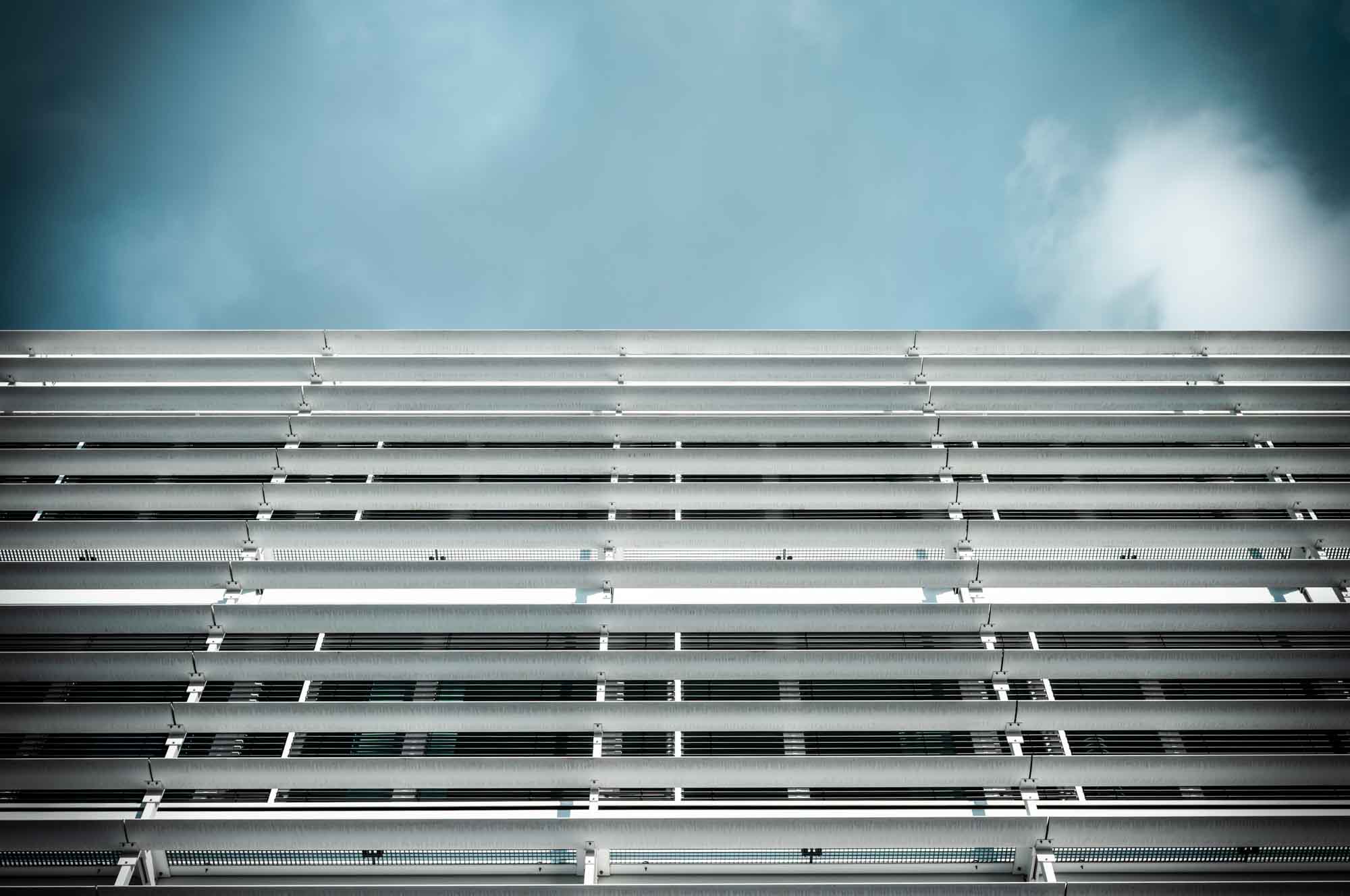 Modern building facade with horizontal metal lines against blue sky, emphasizing architectural symmetry and design.