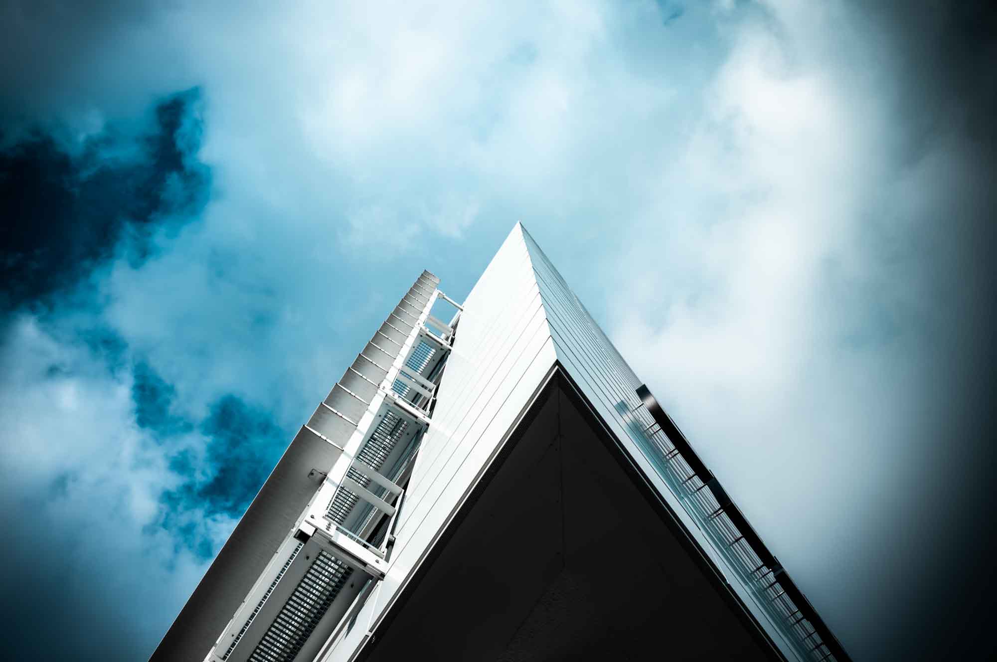 Modern building against a cloudy sky, viewed from below, highlighting its sleek design and architectural lines.