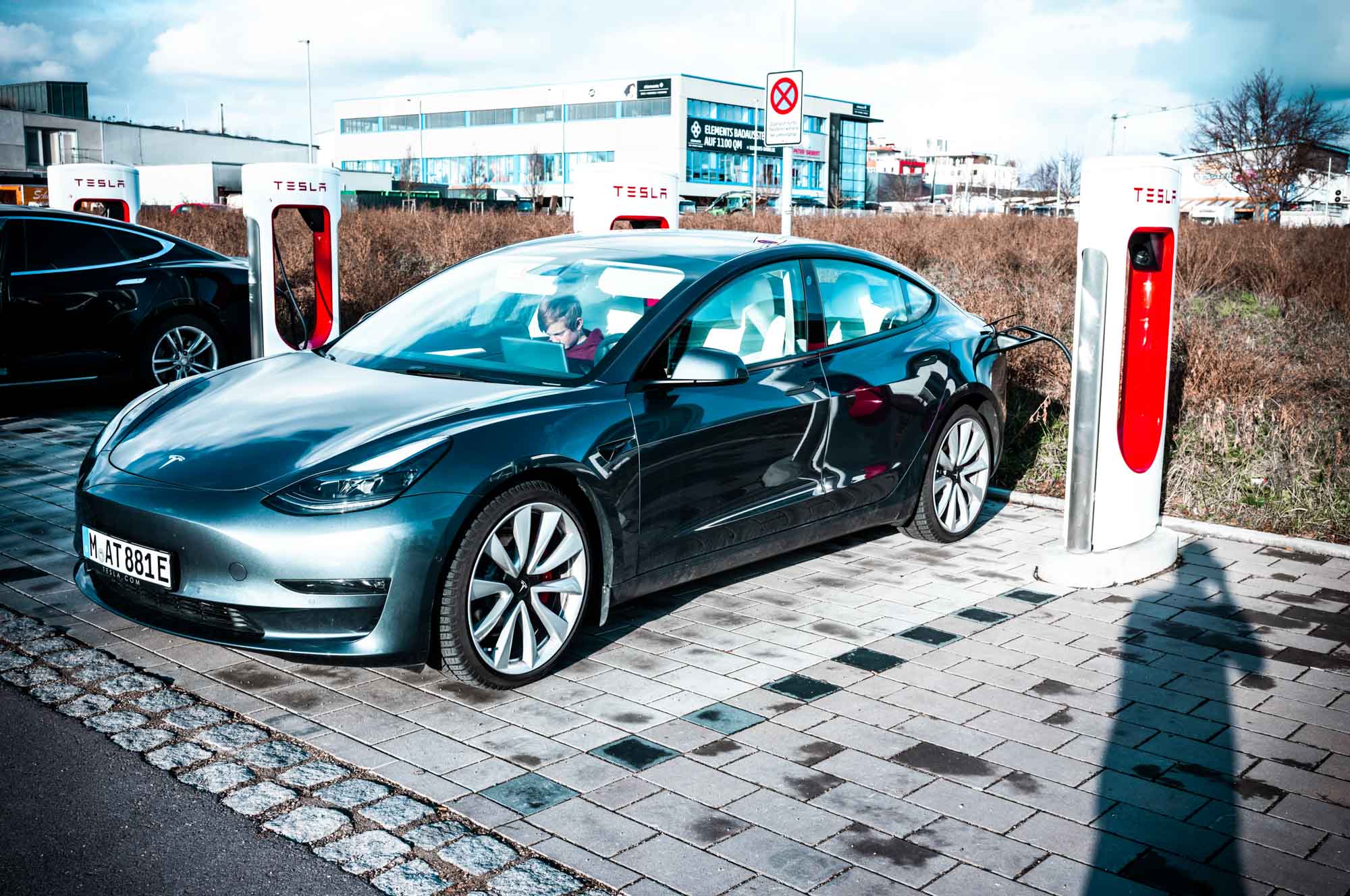 Electric car charging at Tesla Supercharger station on a sunny day.