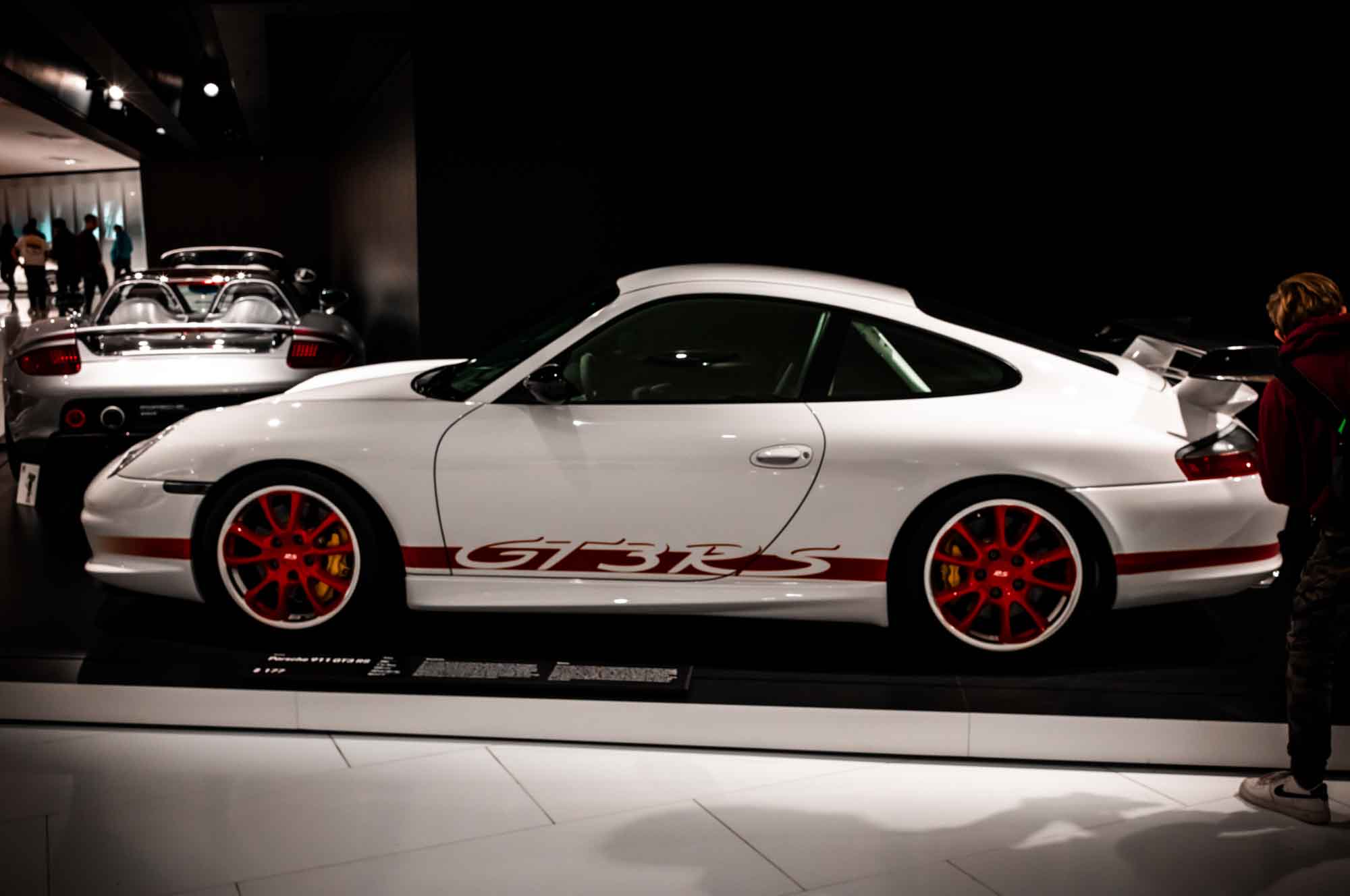 White GT3 RS Porsche showcased in a dimly lit car exhibition, highlighting its sleek design and red accents.