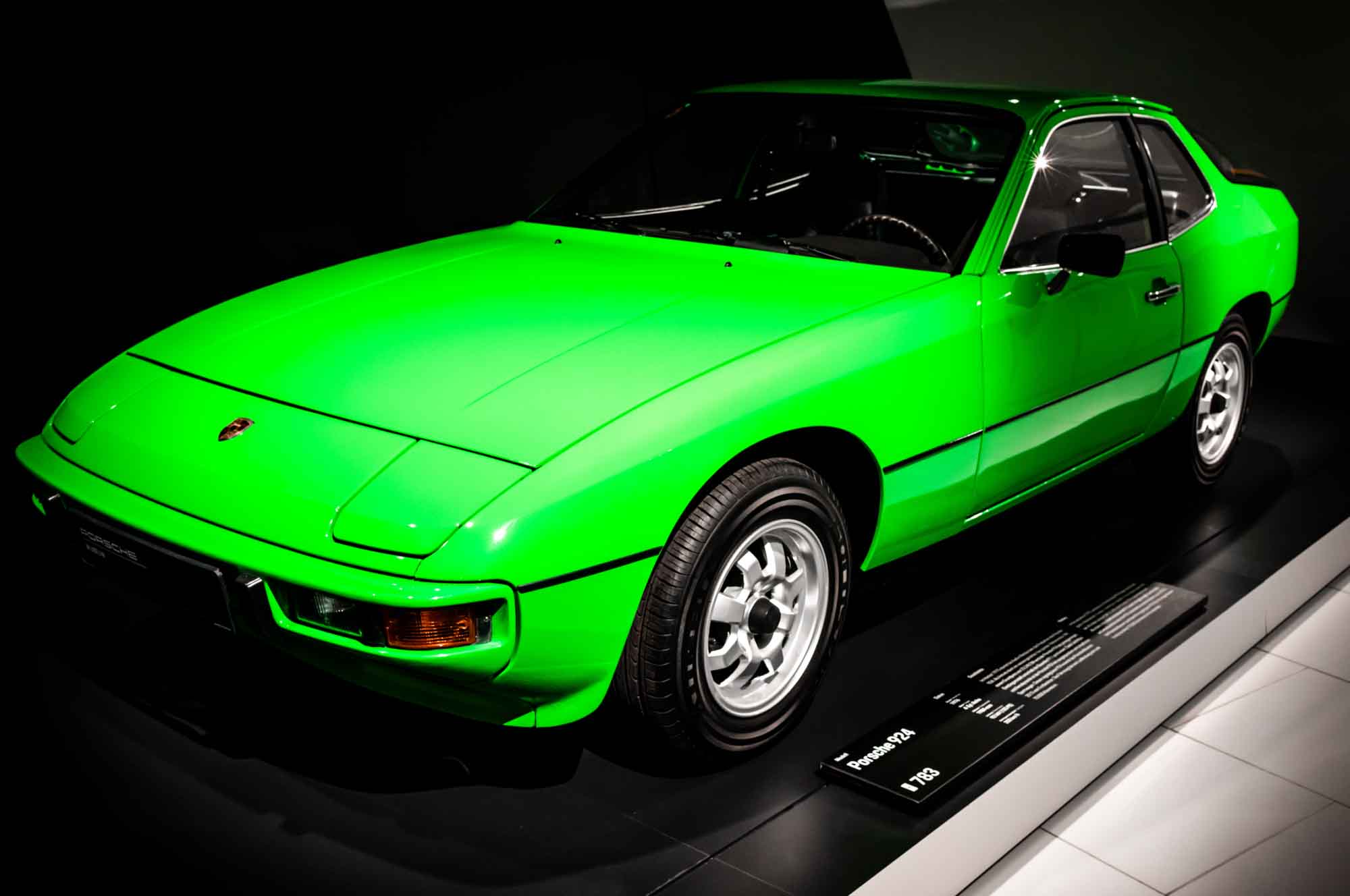 Bright green vintage sports car on display in a museum setting, highlighting sleek design and classic wheels.