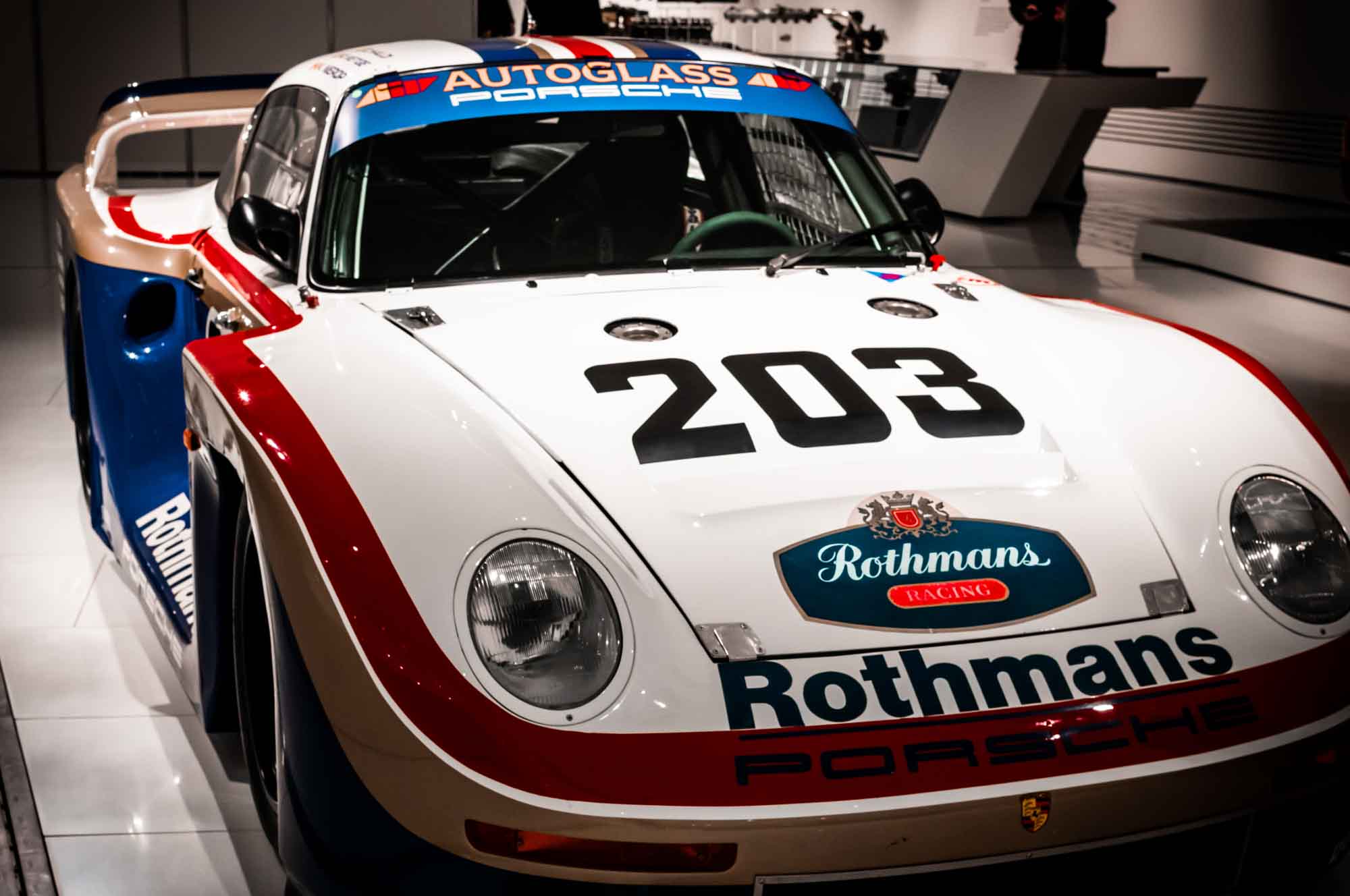Vintage Porsche race car with Rothmans livery showcased in a museum setting.
