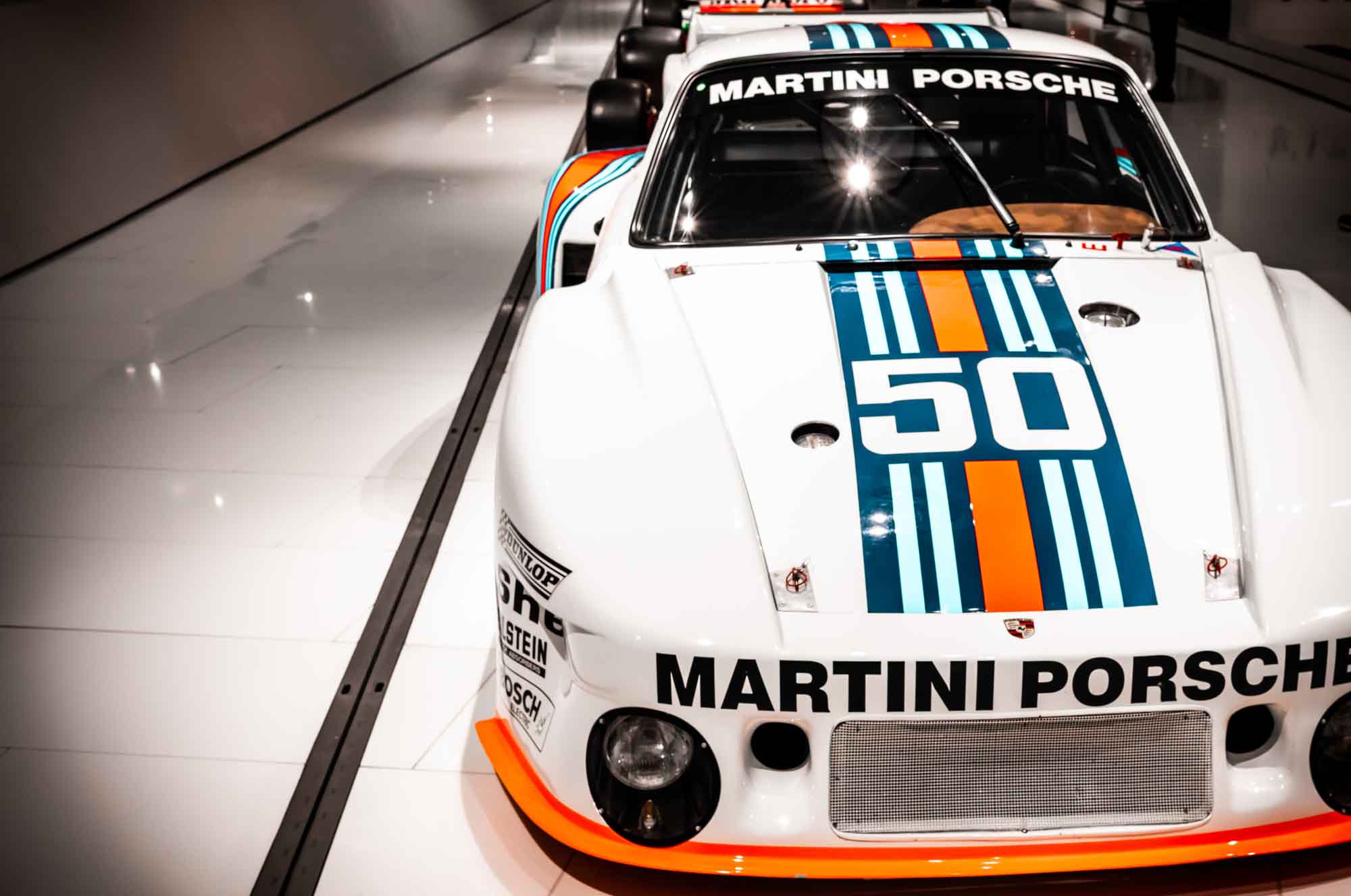 Classic Martini Porsche race car with number 50, featuring iconic blue and orange stripes on a sleek white body.