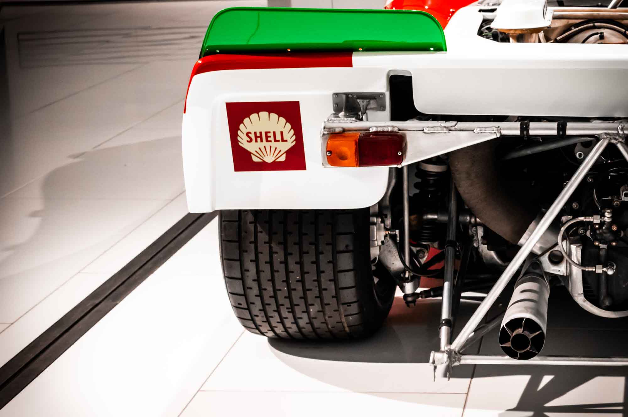 Close-up of vintage race car rear with Shell logo, green spoiler, and visible exhaust details on a white floor.