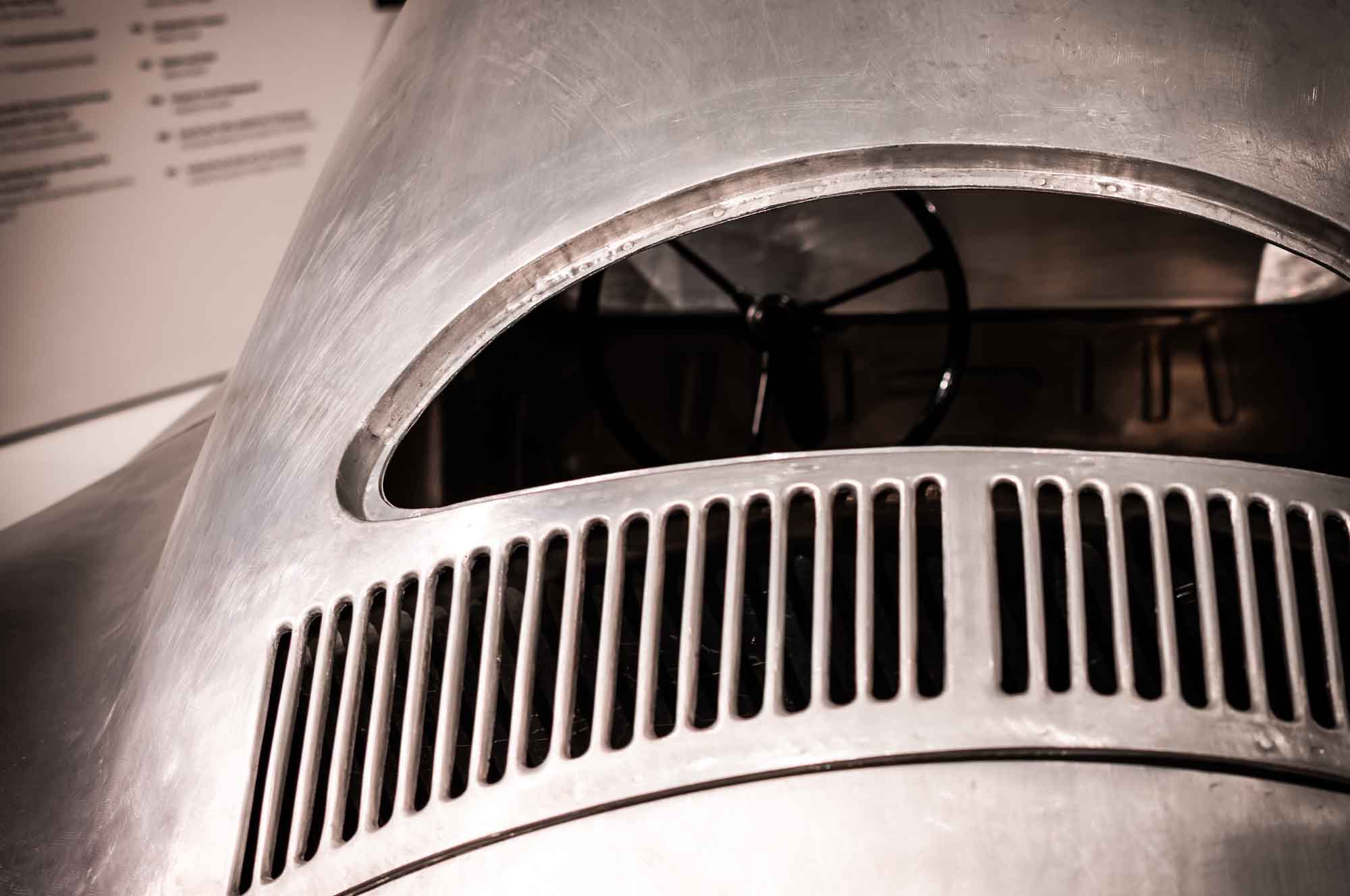 Close-up view of a vintage car's rear engine cover with air vents and visible steering wheel inside.
