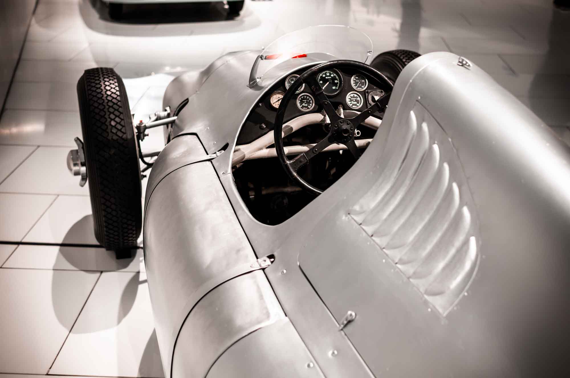 Vintage silver race car with exposed steering wheel and gauges, showcasing classic design and engineering.