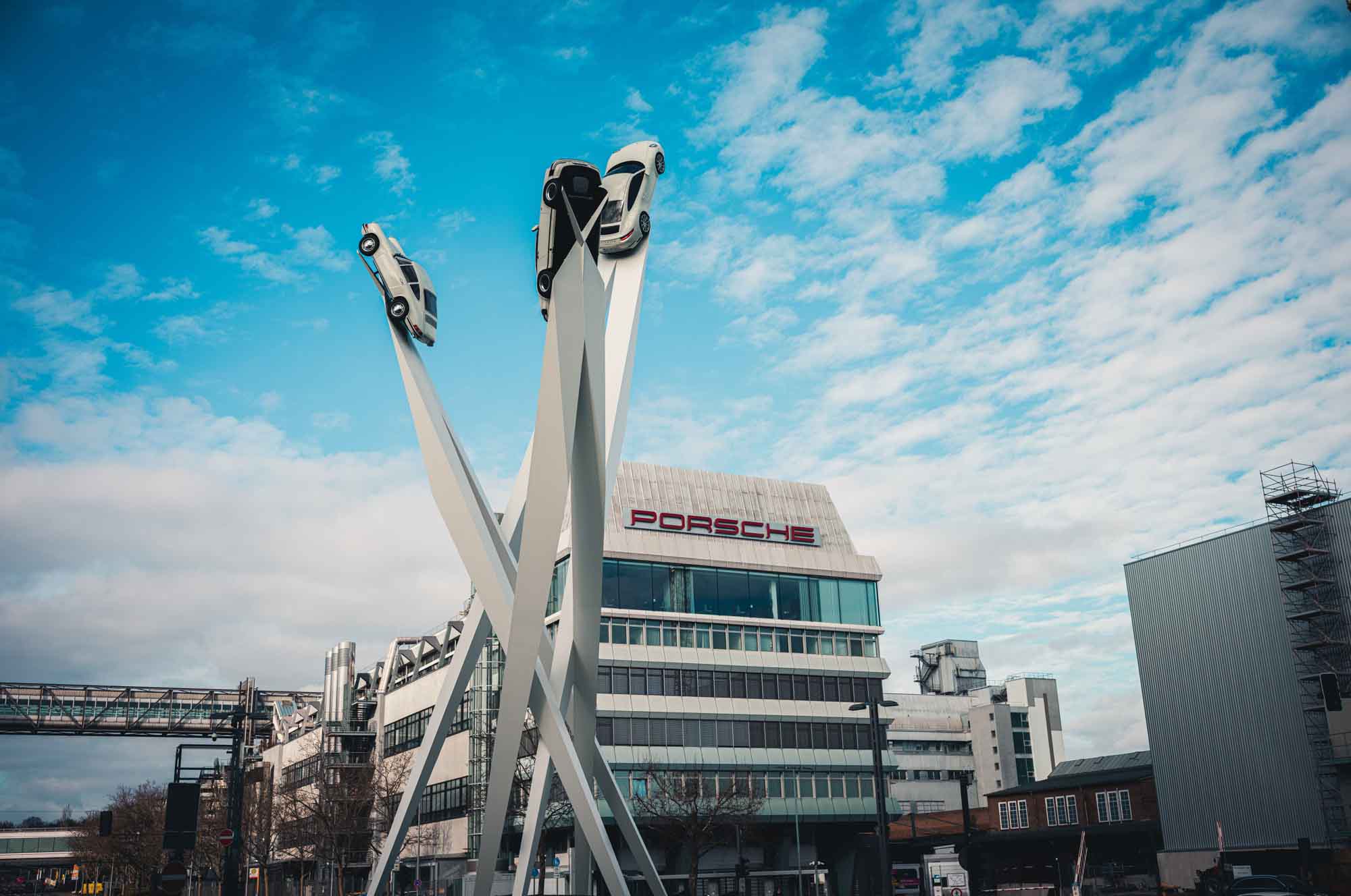 Porsche car sculpture in front of the Porsche Museum, Stuttgart, set against a blue sky with clouds.