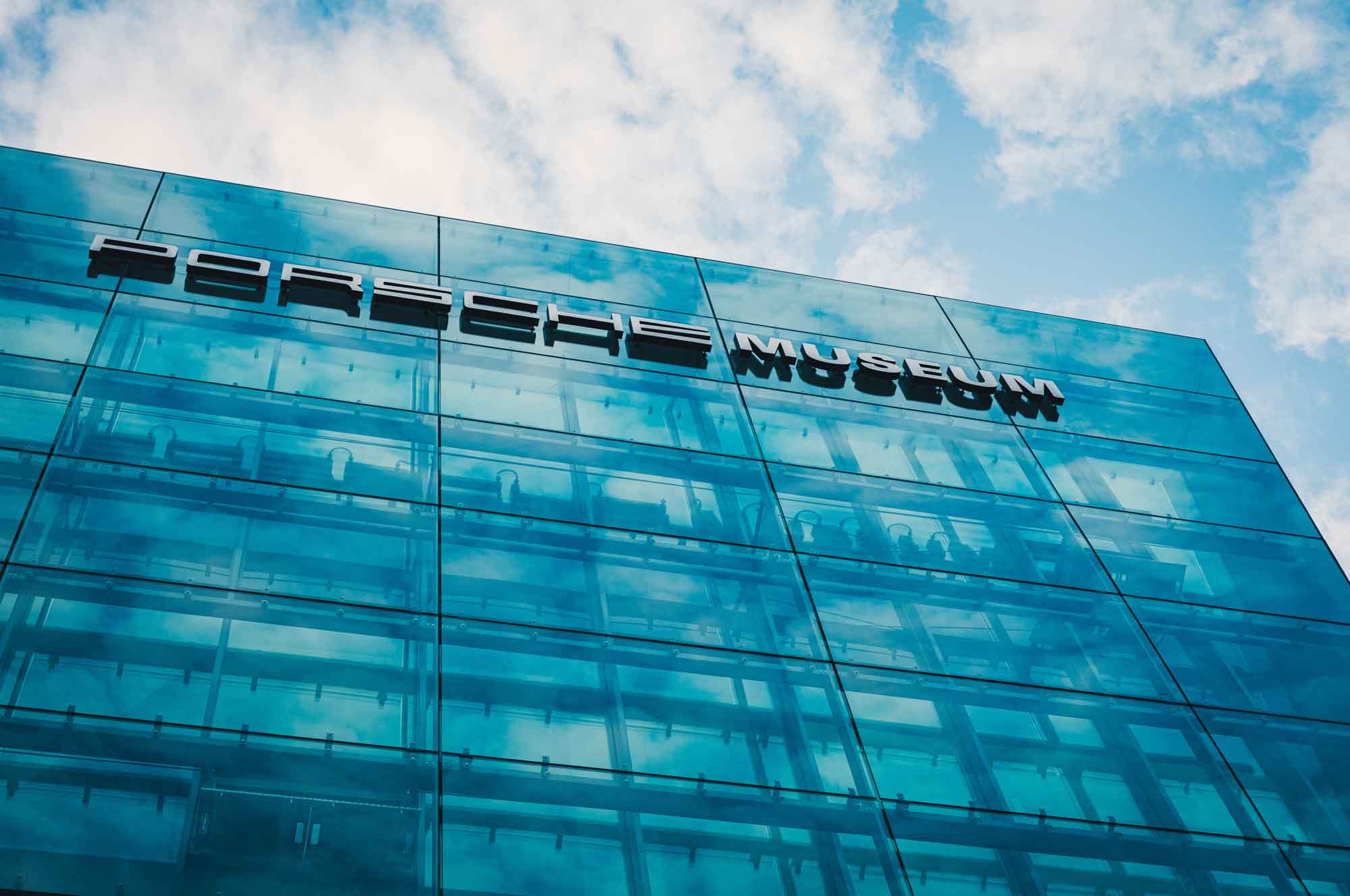 Exterior of the sleek glass facade at the Porsche Museum against a blue sky, showcasing modern architecture.