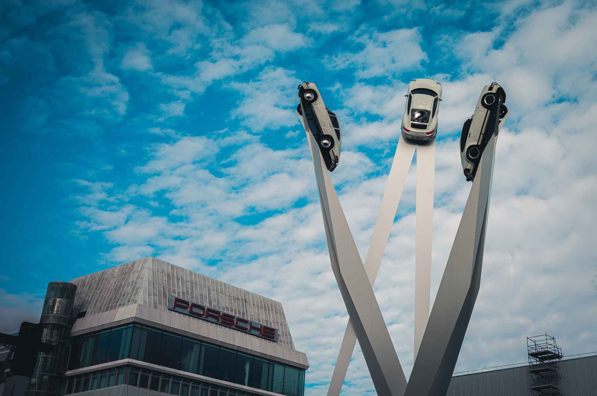 Three classic cars displayed at the Porsche Museum against a cloudy sky.