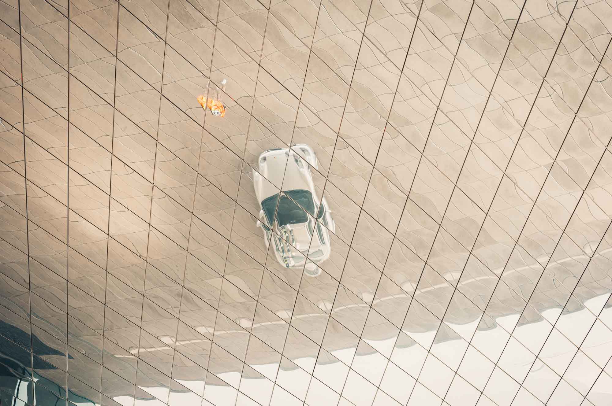 Reflection of a futuristic car hanging indoors on a wavy mirrored ceiling, creating an artistic optical illusion.