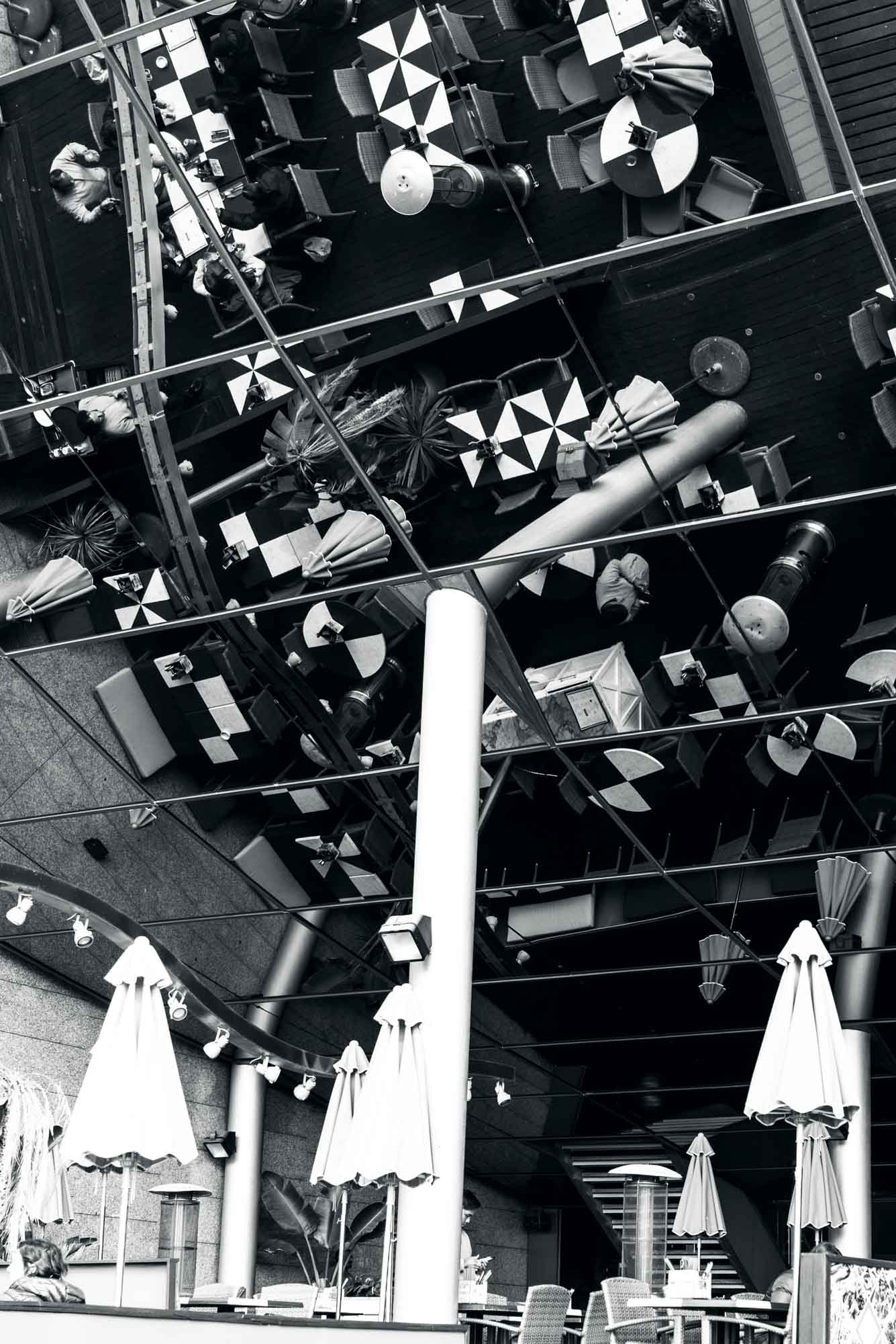Abstract black and white view of cafe tables and chairs reflected on mirrored ceiling.