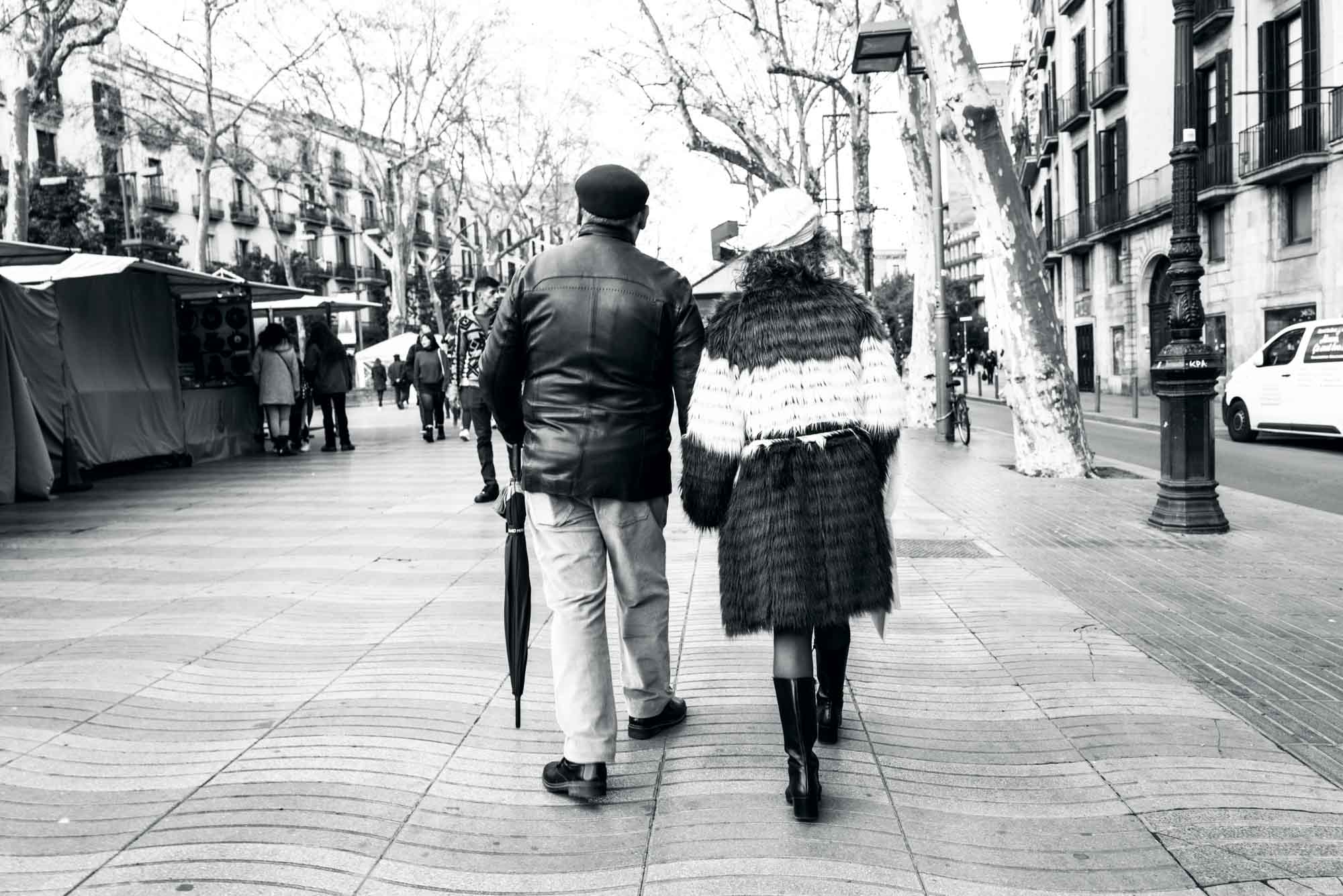 Elderly couple walking arm in arm on a city street, wearing stylish winter clothing.