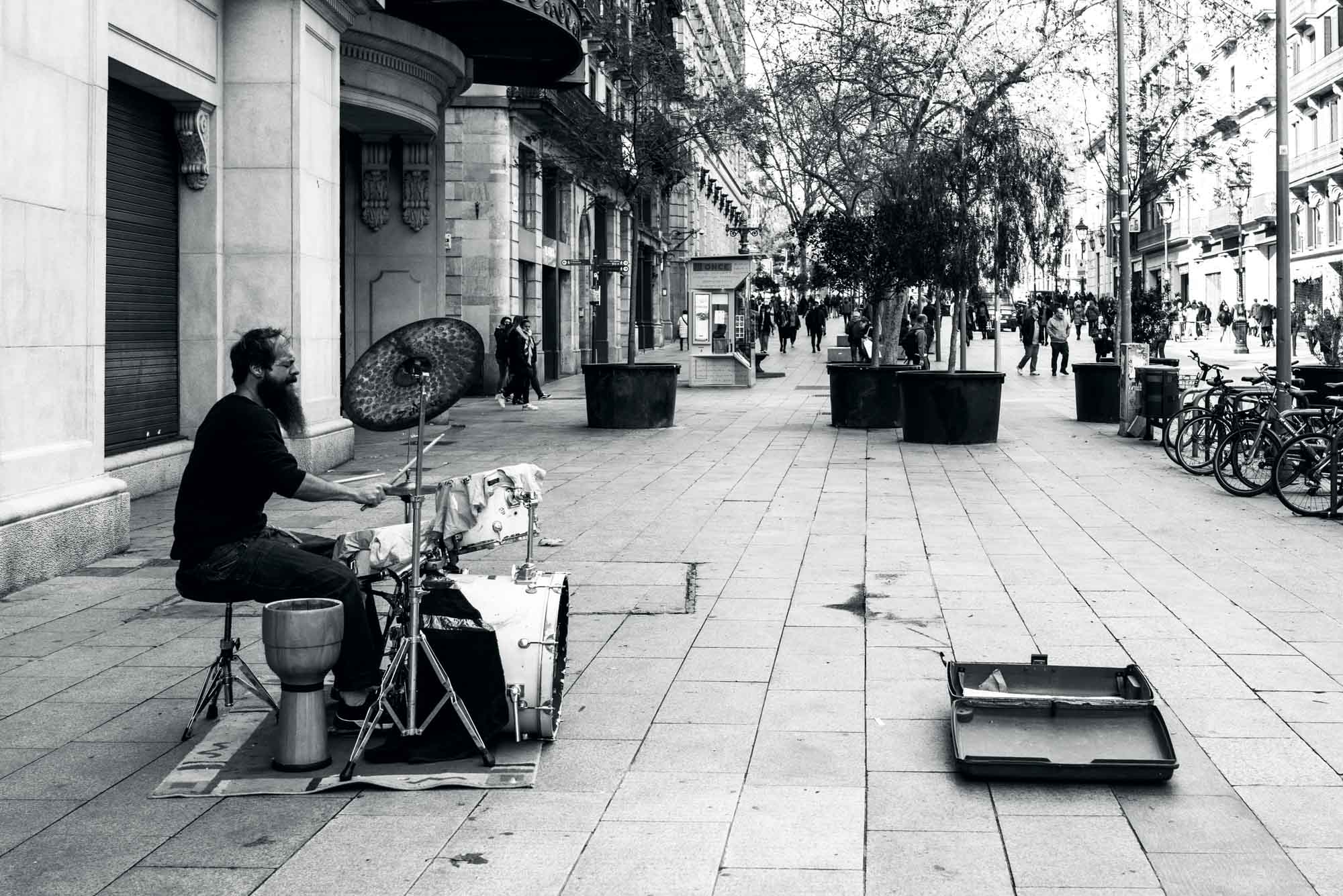Street drummer performing for passersby in a city plaza, black and white photo.