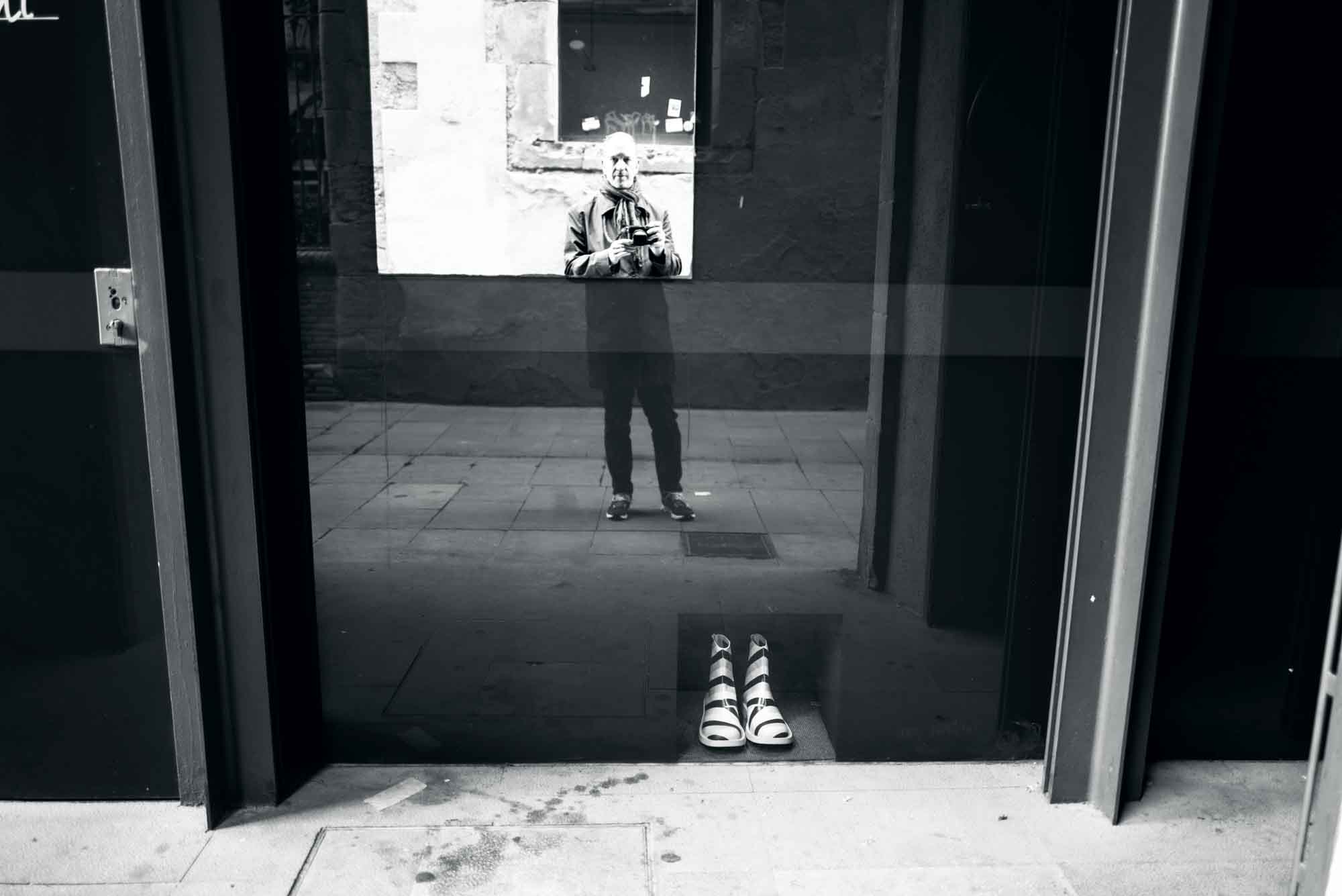 Reflection in a window with empty sandals on the ground, creating a mysterious and artistic street scene.