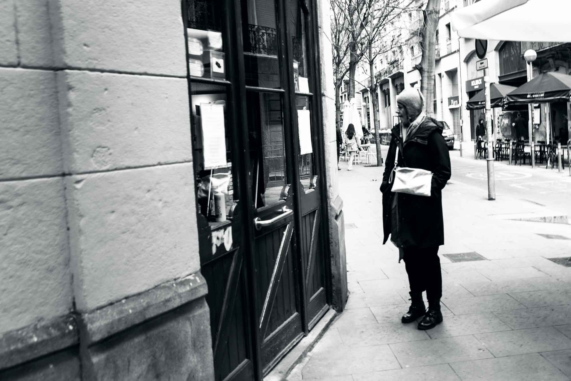 Person in coat looking at a storefront window on an empty city street.