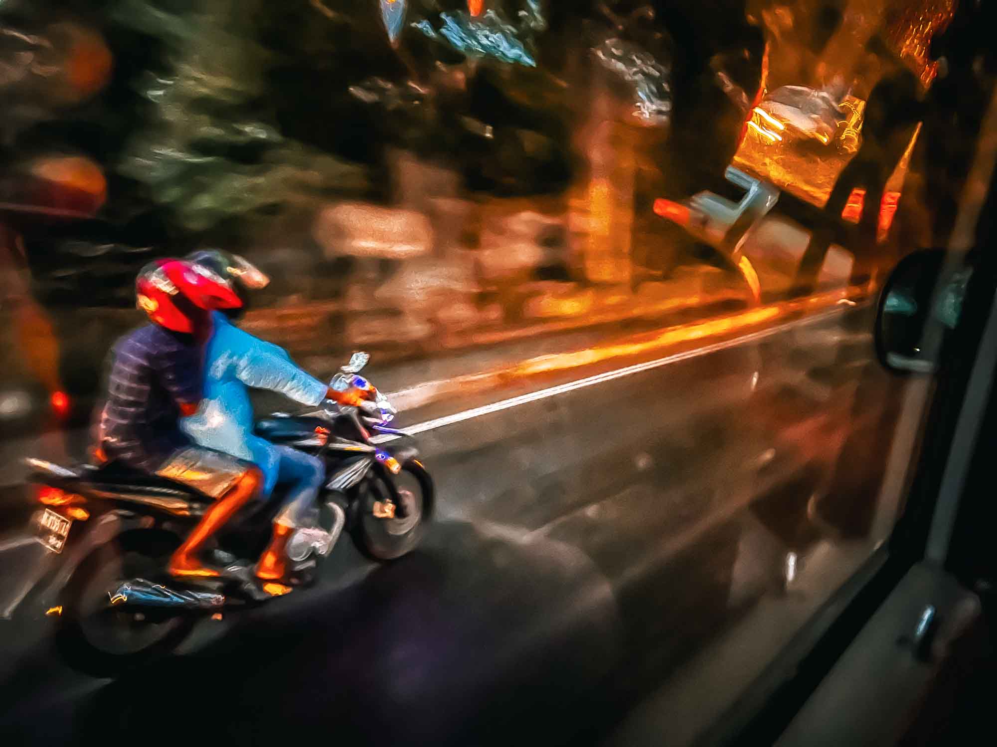 Two people on a motorcycle riding in the rain, blurred motion with vibrant lights reflecting on wet street at night.