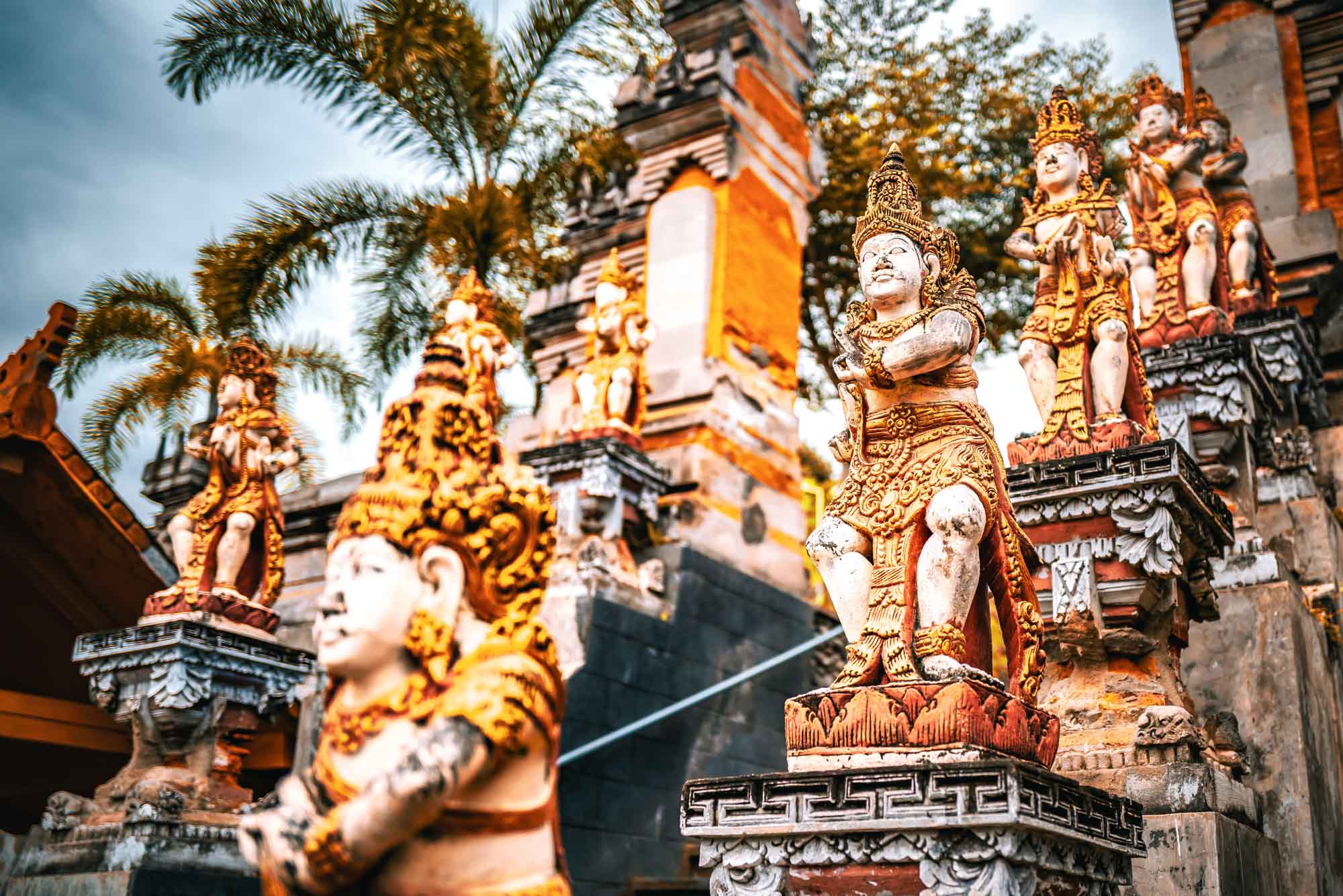 Ornate Balinese temple statues with vibrant colors and intricate carvings, surrounded by tropical palm trees.