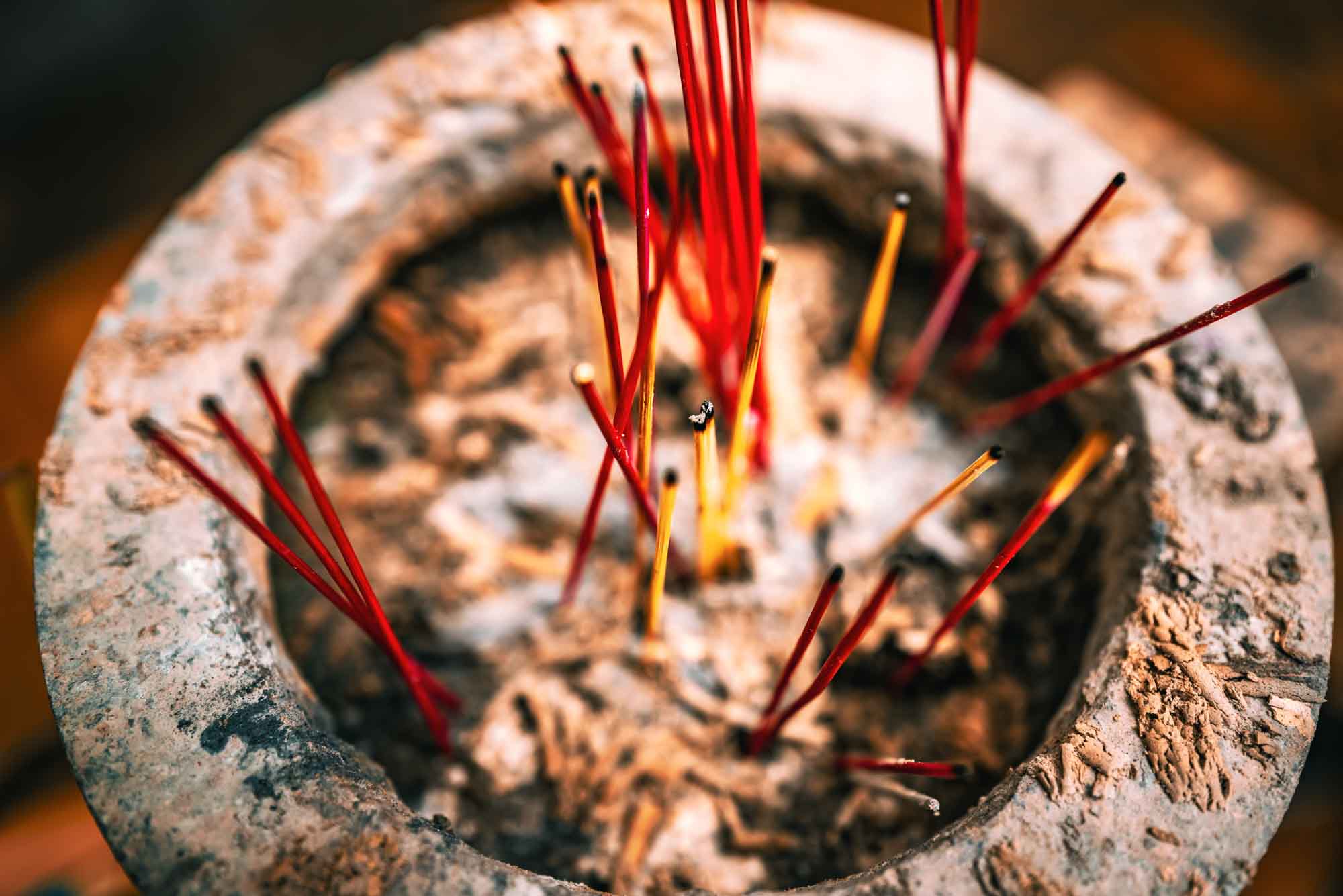 Red incense sticks in a rustic pot, surrounded by ash, creating a serene and spiritual atmosphere.