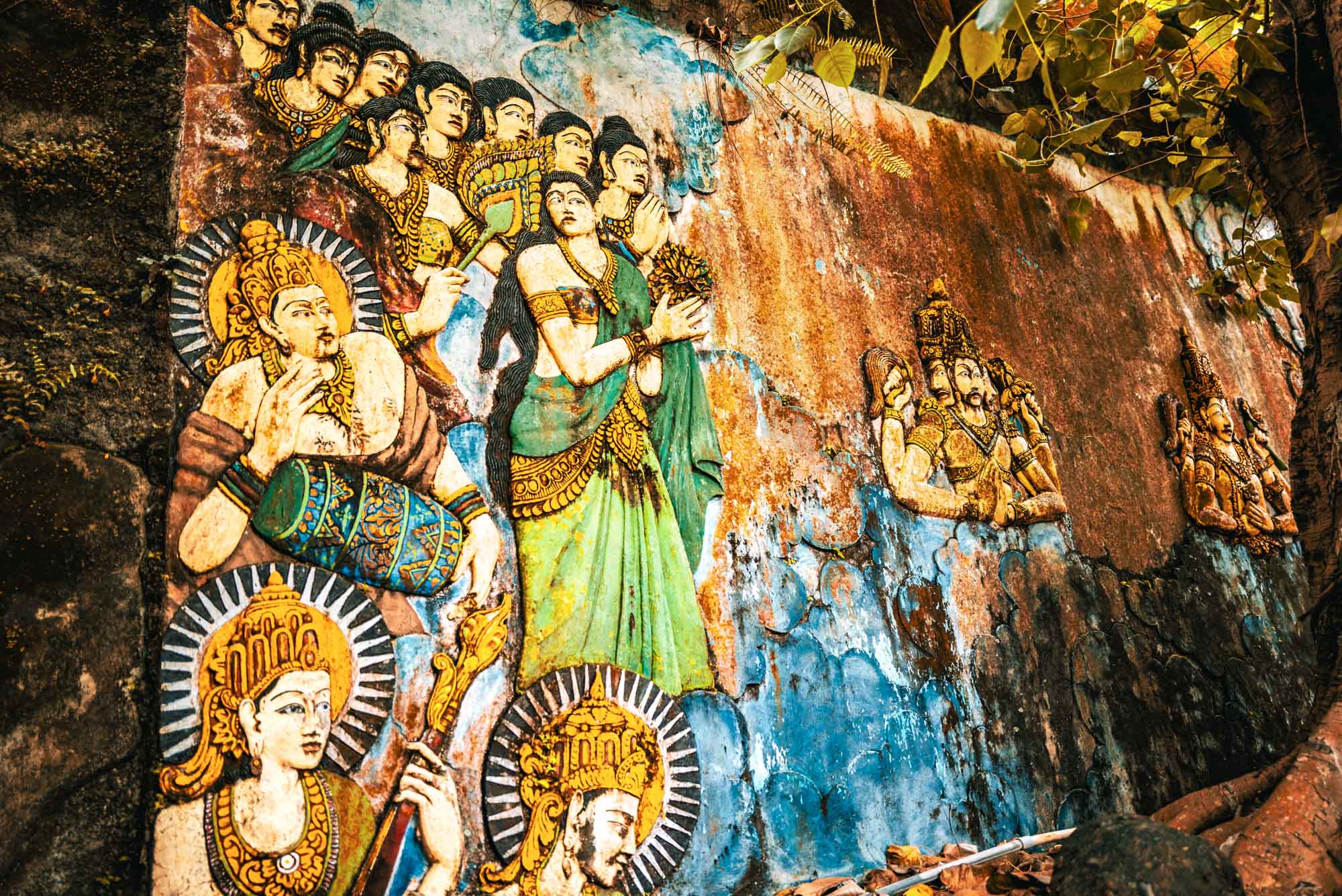 Ancient Indian mural depicting mythological figures in vivid colors on a textured stone wall.