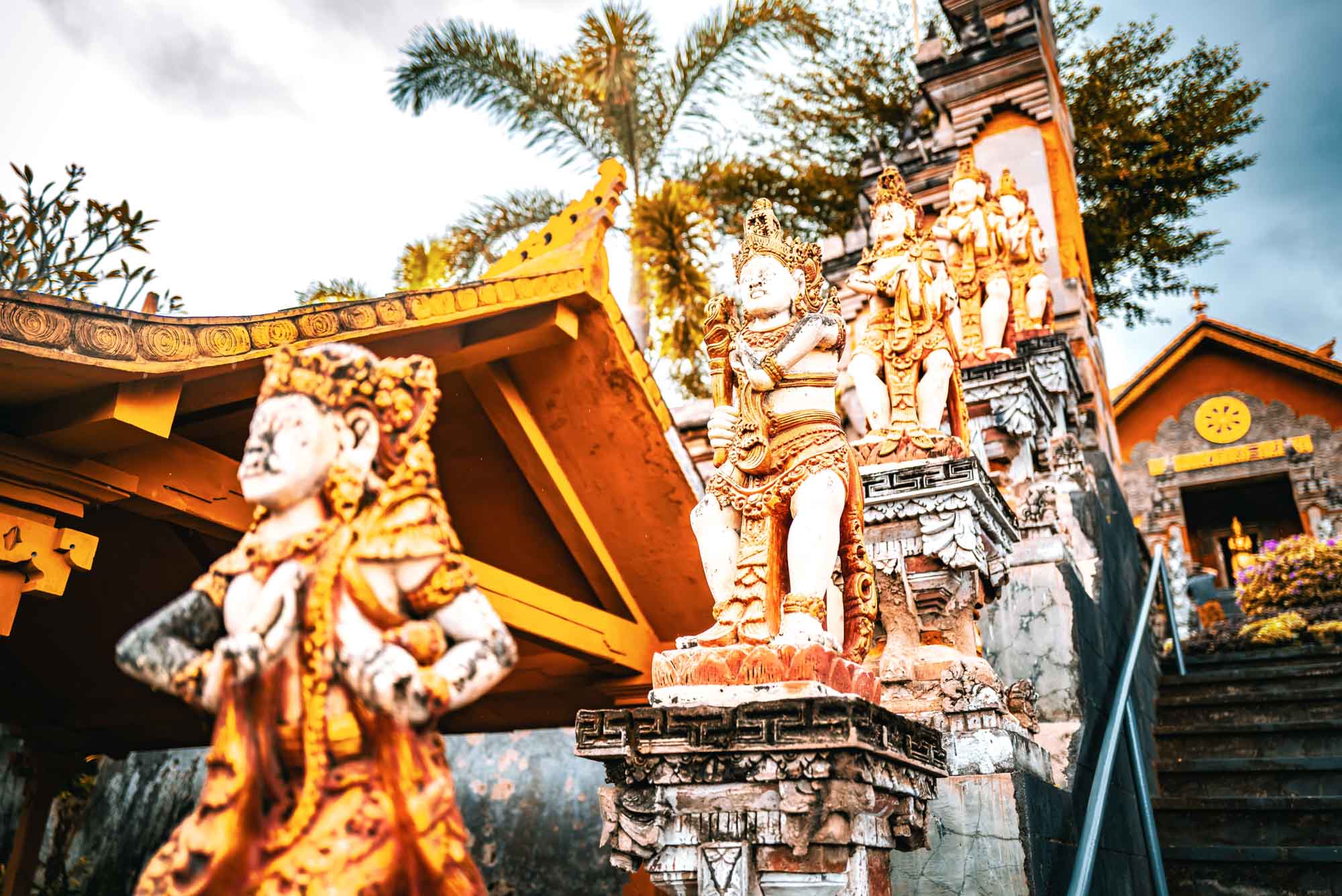 Colorful stone statues on temple steps, surrounded by tropical foliage, under a bright sky.