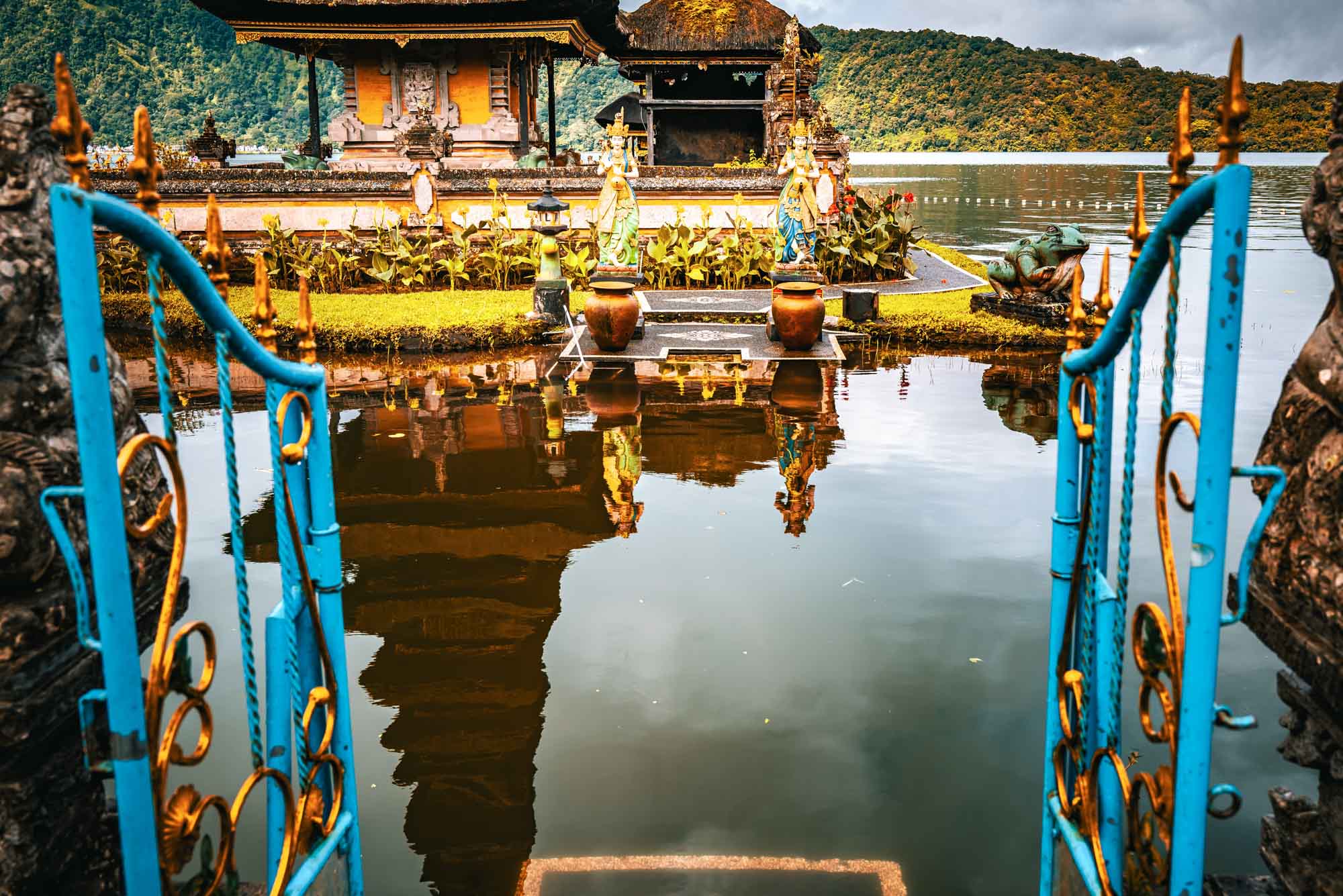 Colorful temple reflection in water, framed by ornate blue and gold gate in Bali, Indonesia.