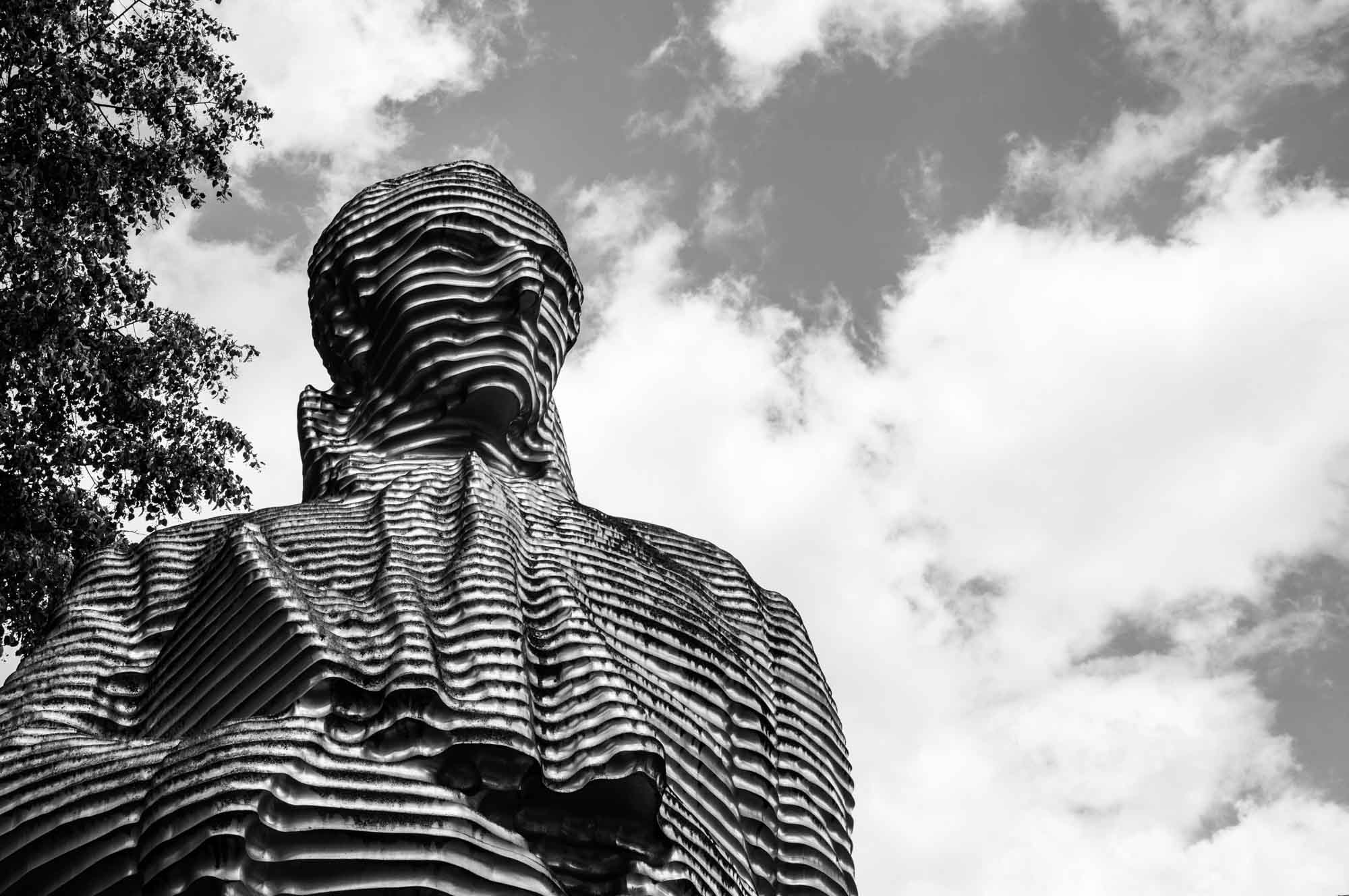 Layered metal statue against a cloudy sky, artistic sculpture with unique texture. Black and white photography.