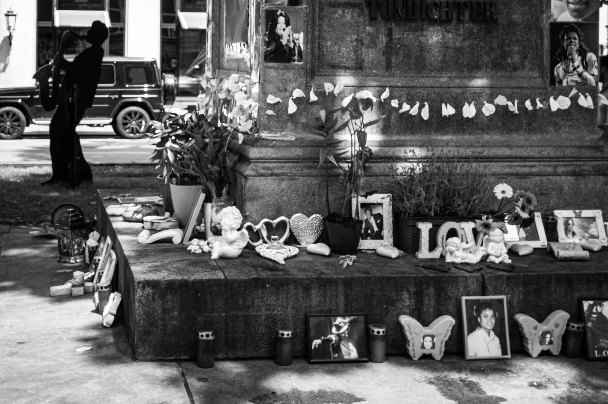 Street memorial adorned with flowers, candles, photos, and heartfelt tributes in black and white.