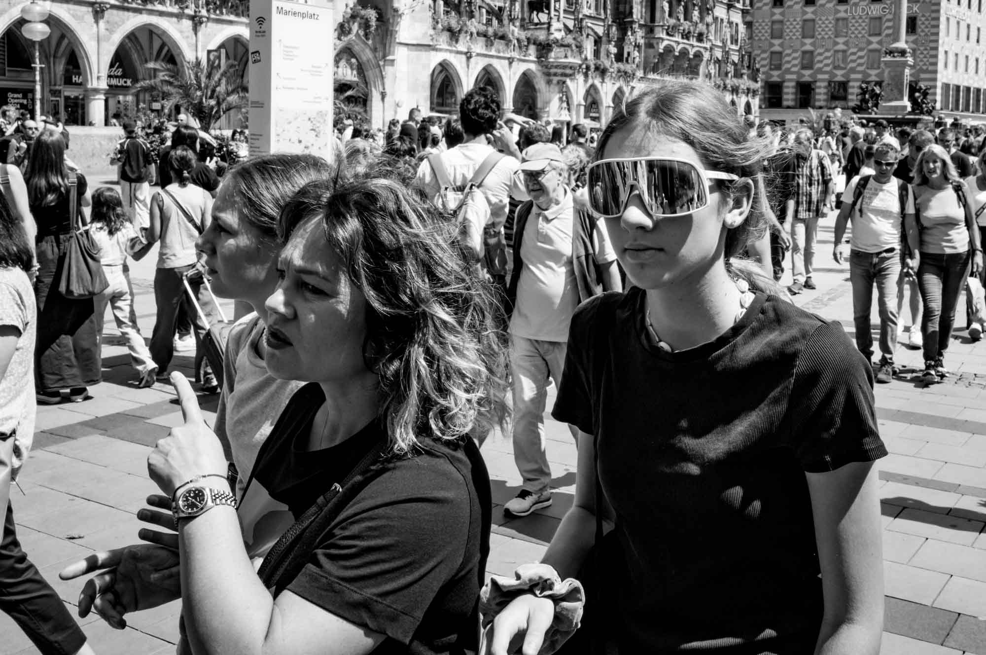 Crowded Marienplatz in Munich with two women walking in foreground, one pointing, others exploring in the background.