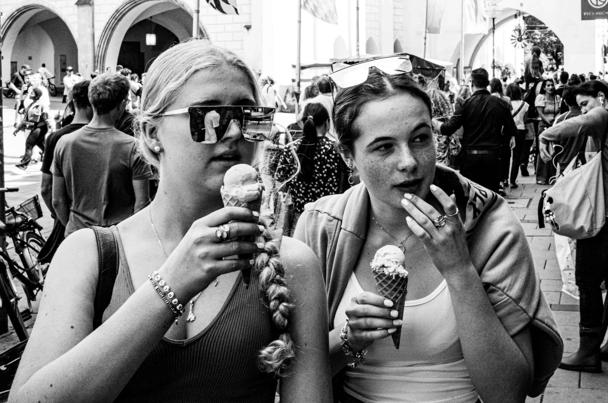 Two people enjoying ice cream cones on a busy street, surrounded by a lively crowd. Black and white photo.