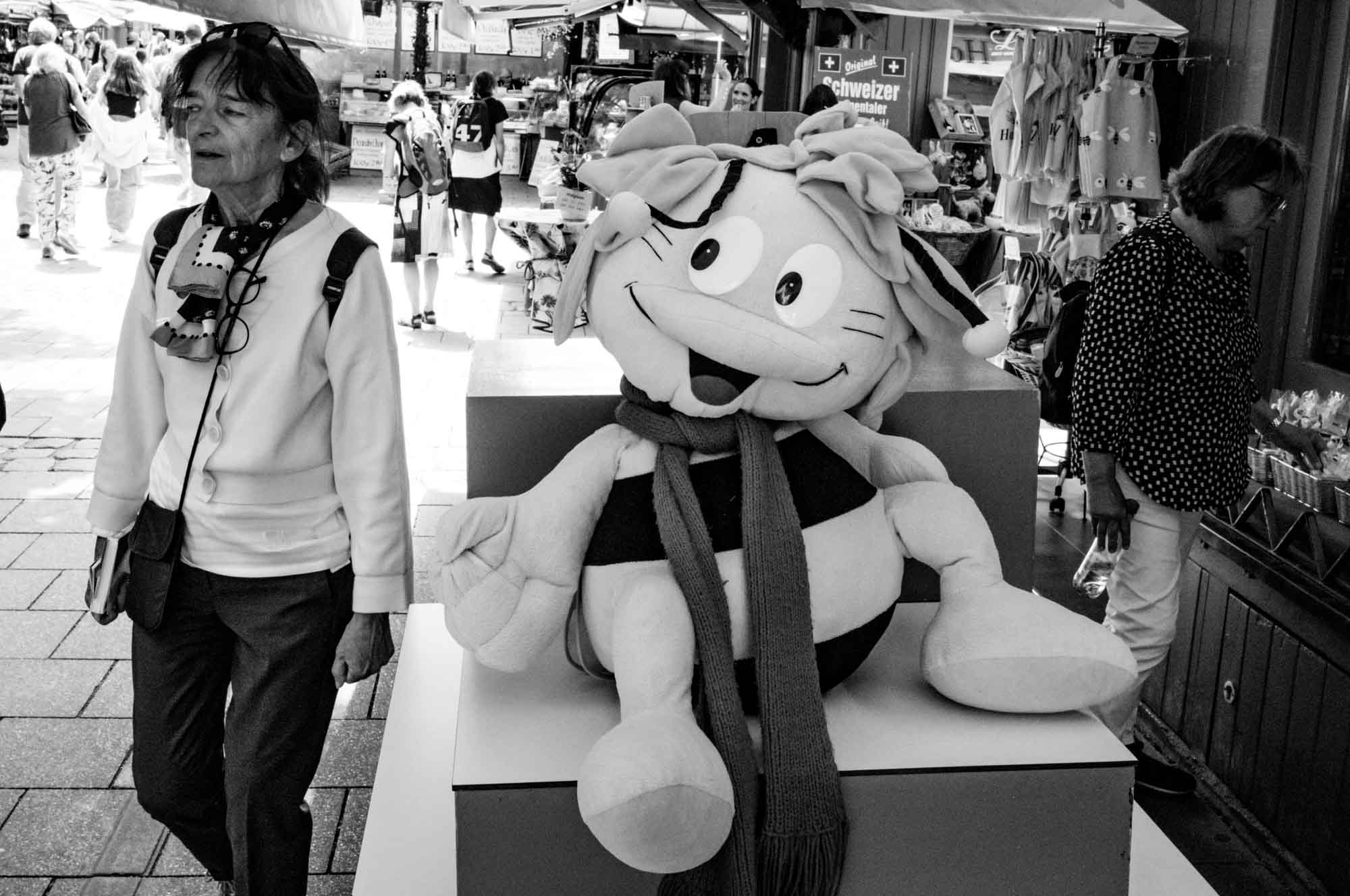 Plush toy in a market setting with people walking by, showcasing a lively street atmosphere.