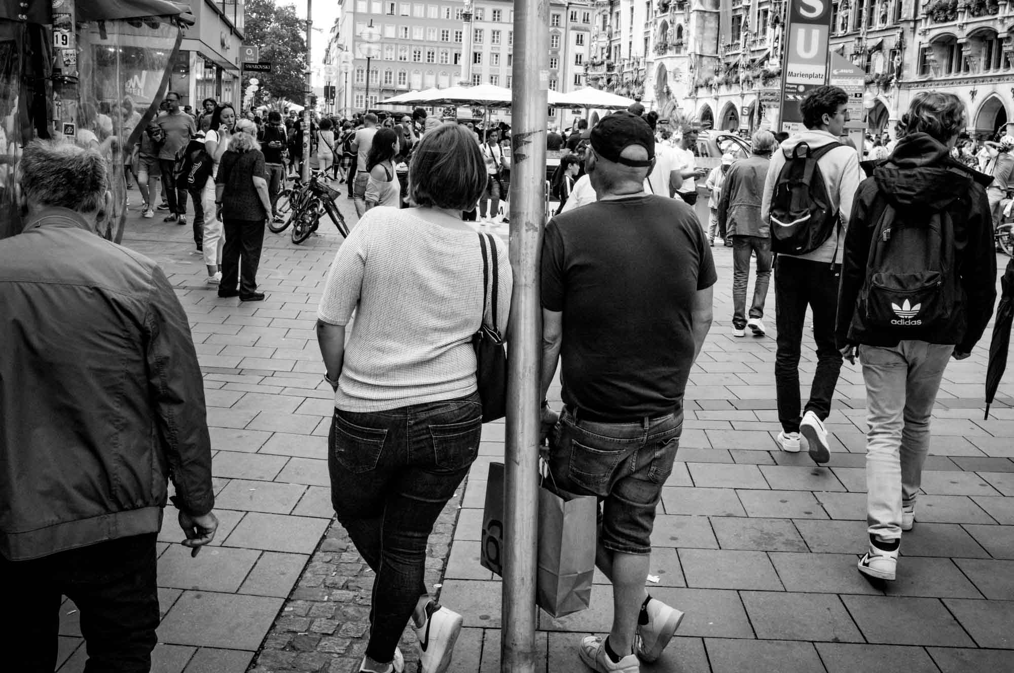 Black and white city scene with people walking and standing near a busy square.