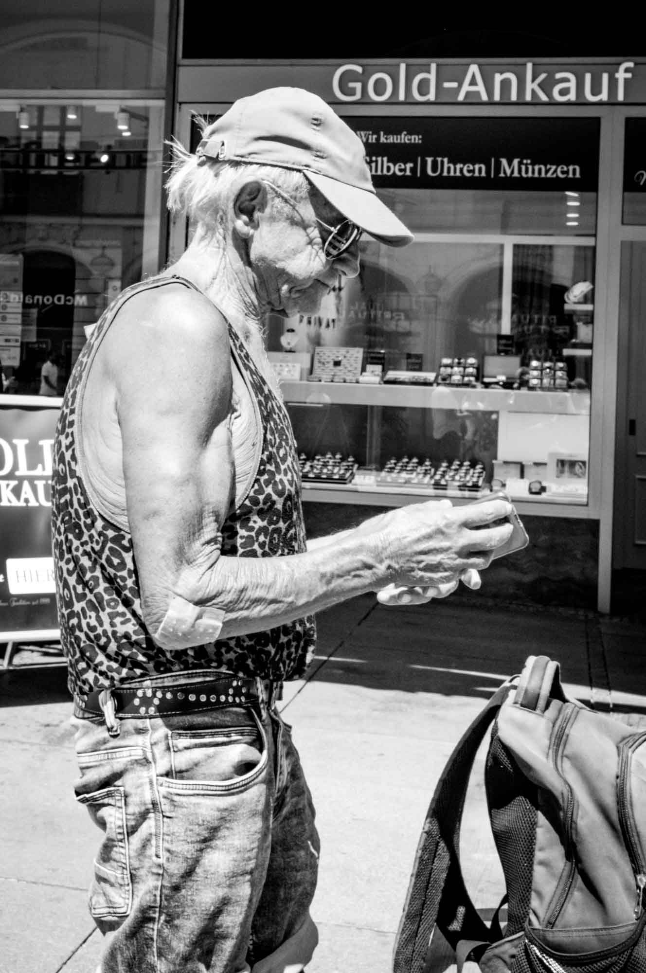 Man in tank top using smartphone outside a shop.