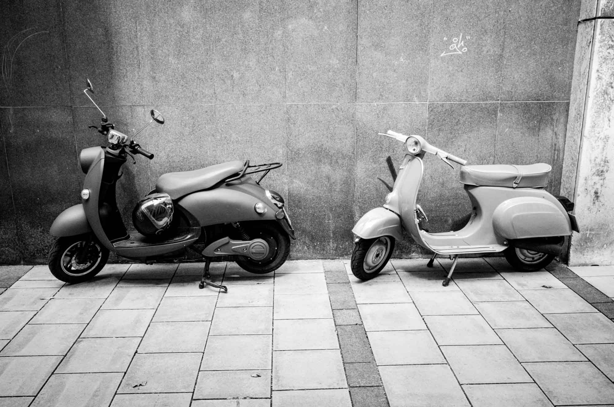 Two vintage scooters parked side by side against a textured wall, showcasing classic design.