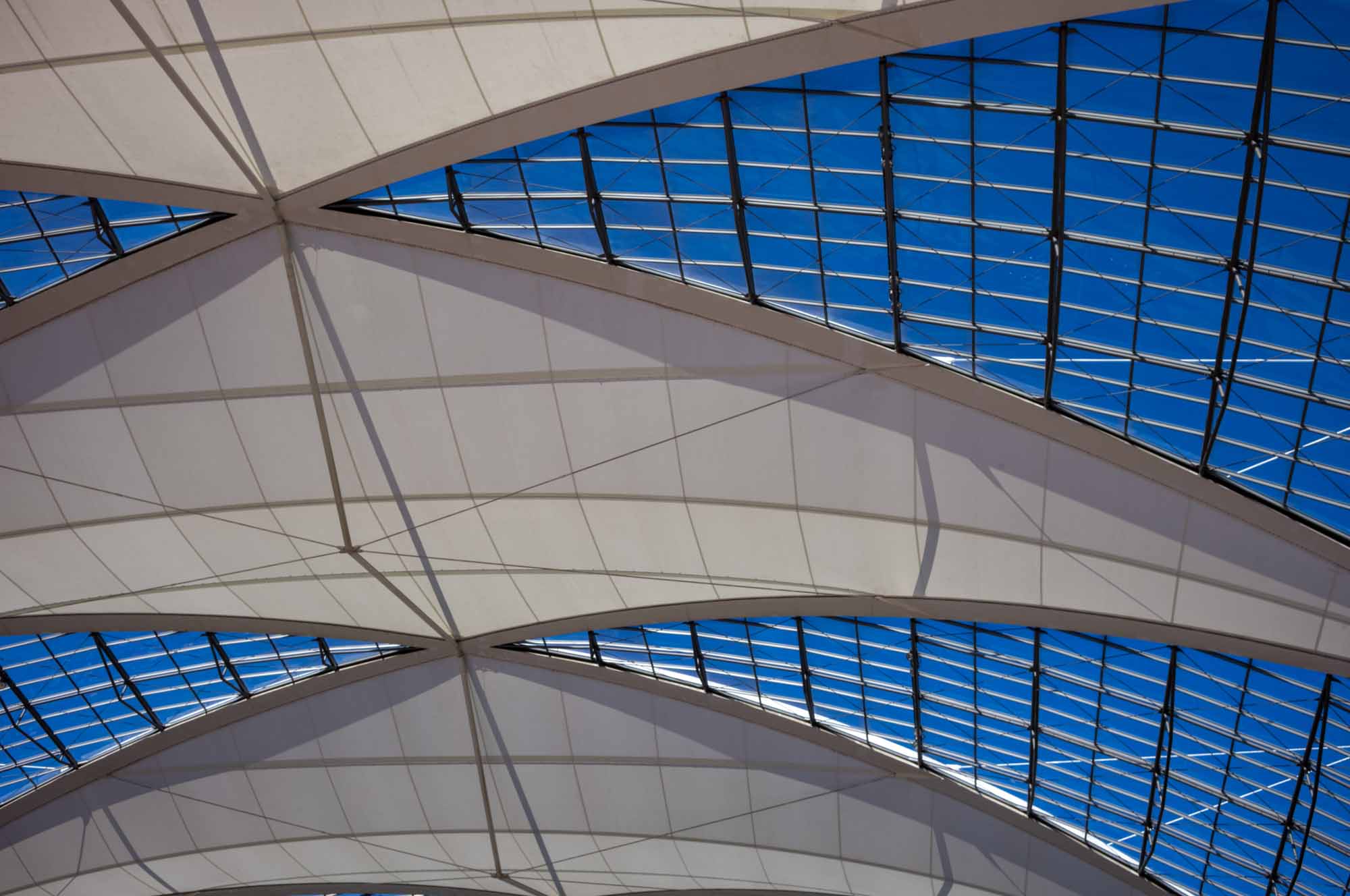 Modern architectural roof design with curved glass panels against a clear blue sky.