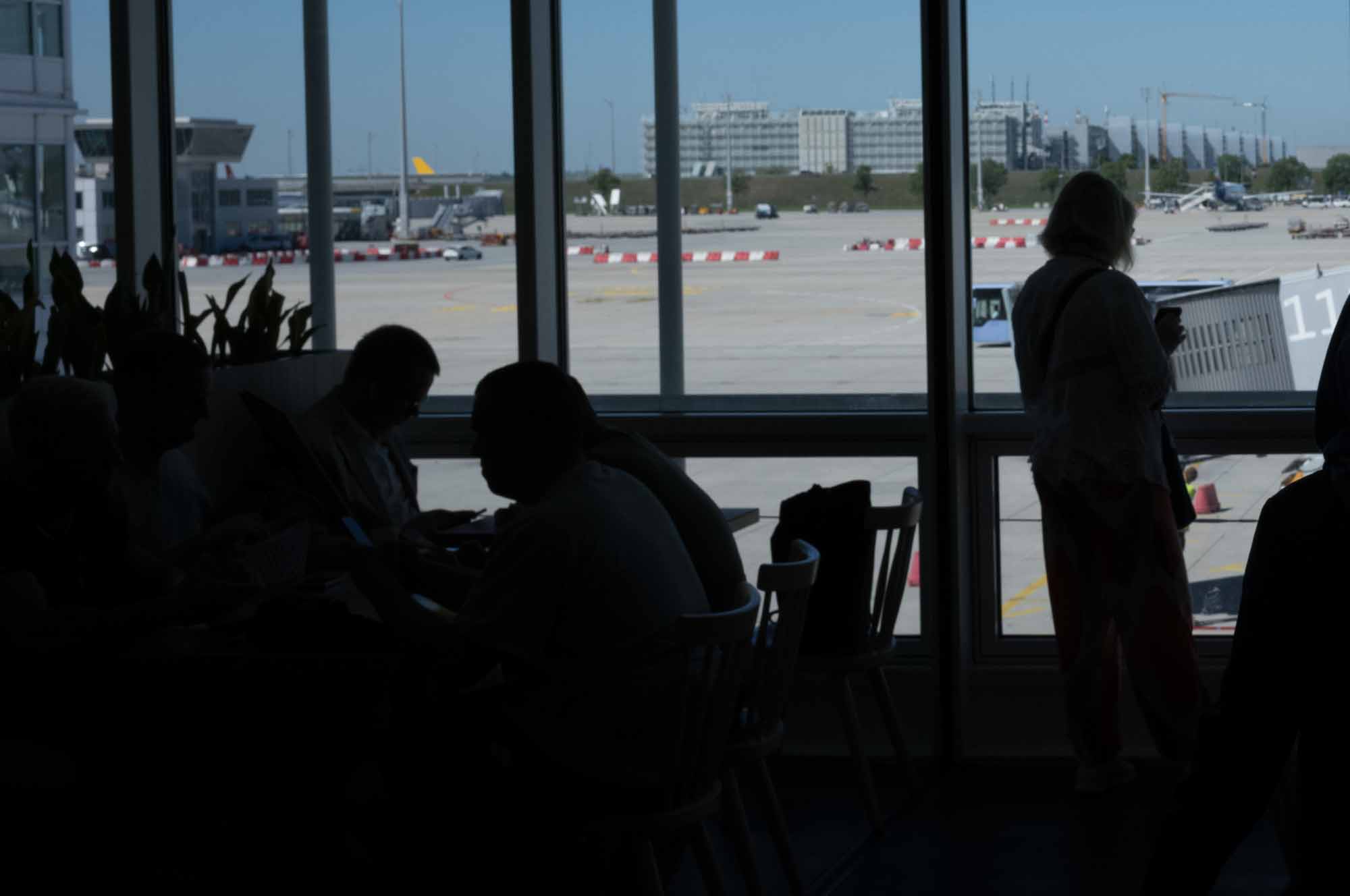 People seated near an airport window, overlooking the runway and preparing for travel.