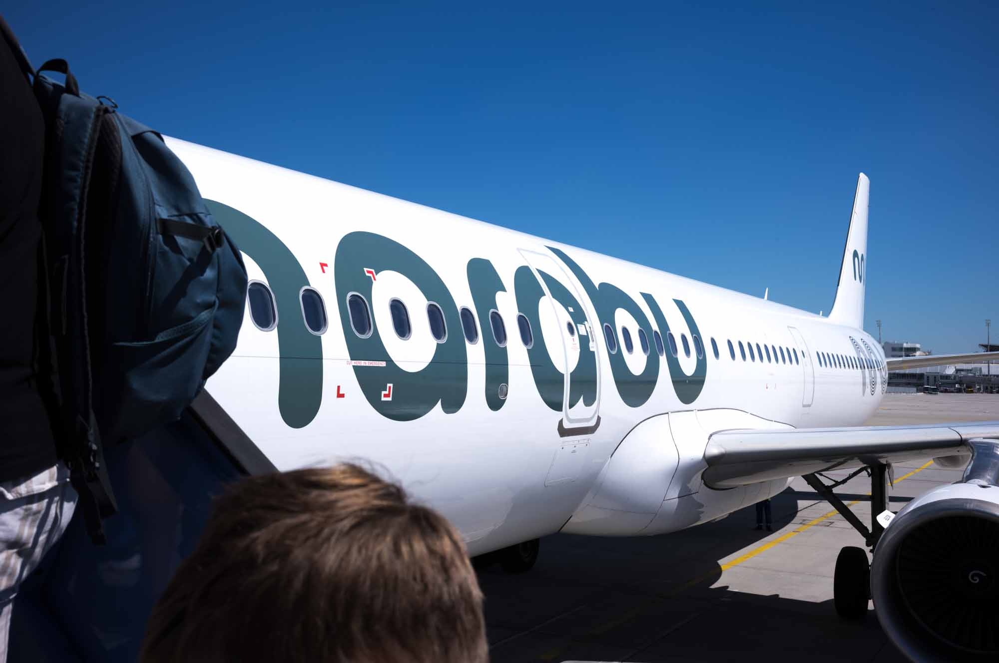 Airplane on tarmac with boarding passengers under clear blue sky.