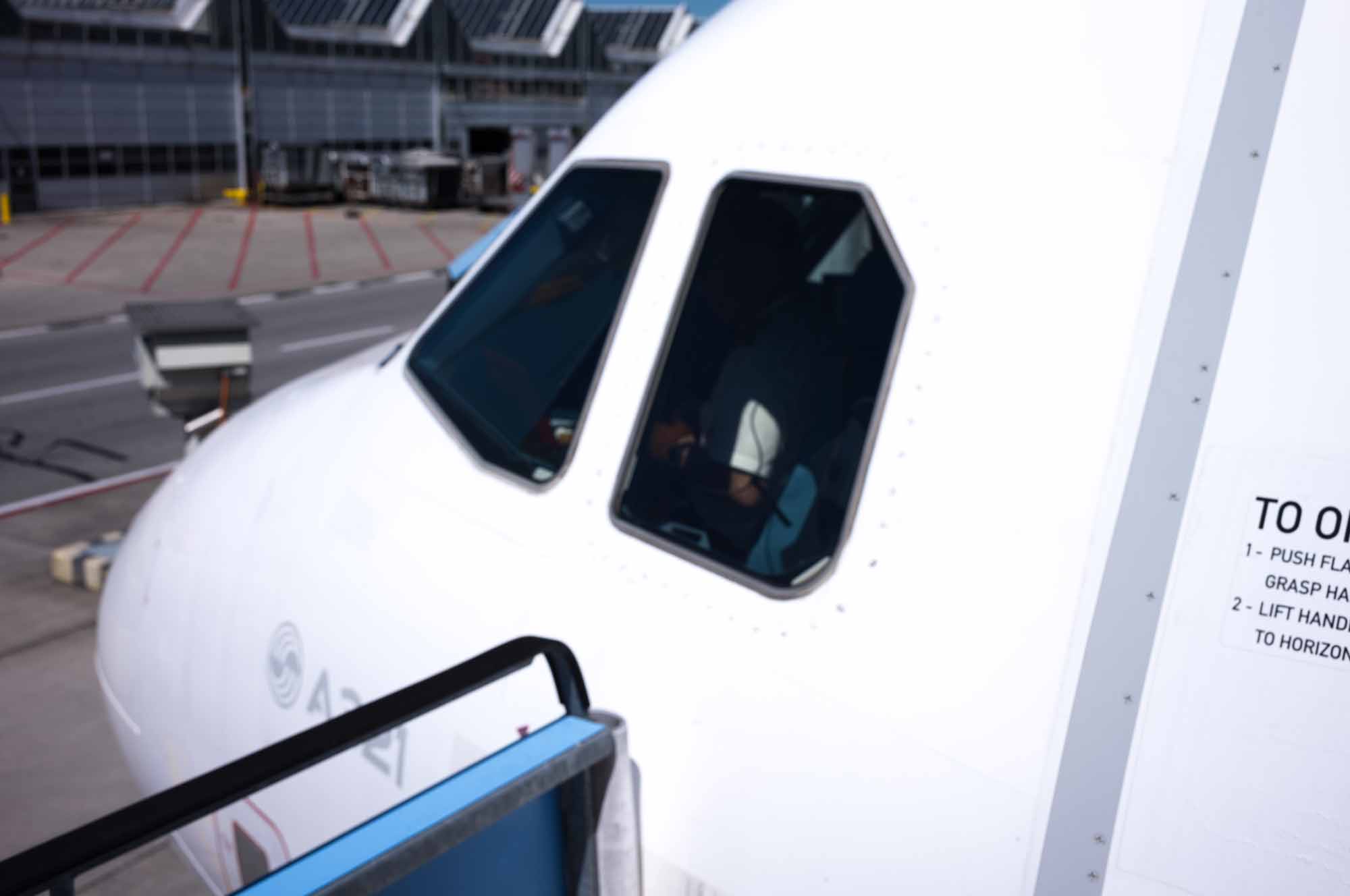Close-up of airplane cockpit with pilot sitting, parked at airport terminal.