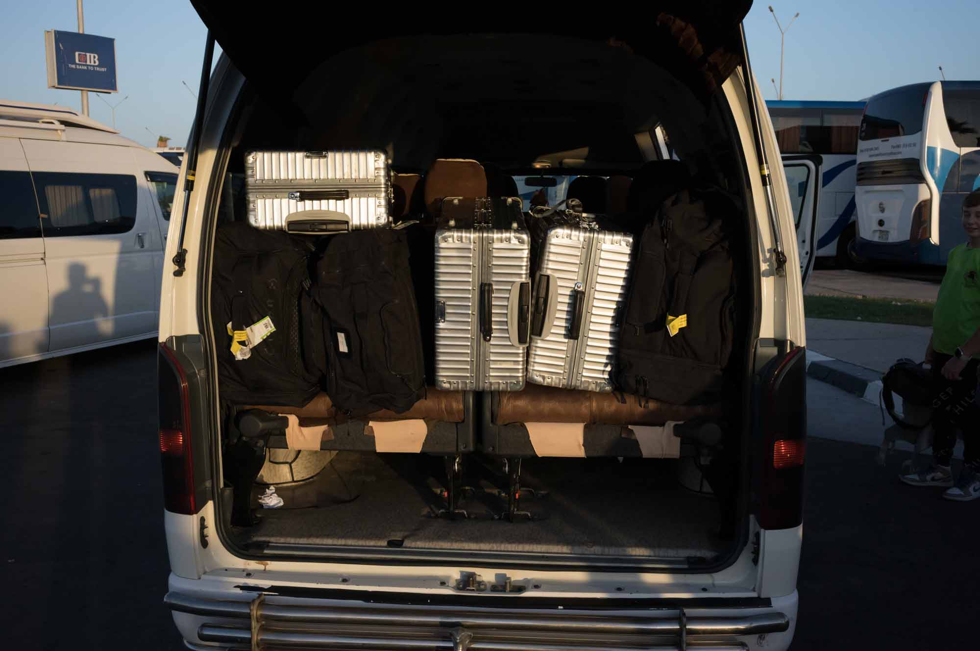 Van loaded with silver suitcases and black bags at a transport station during evening.