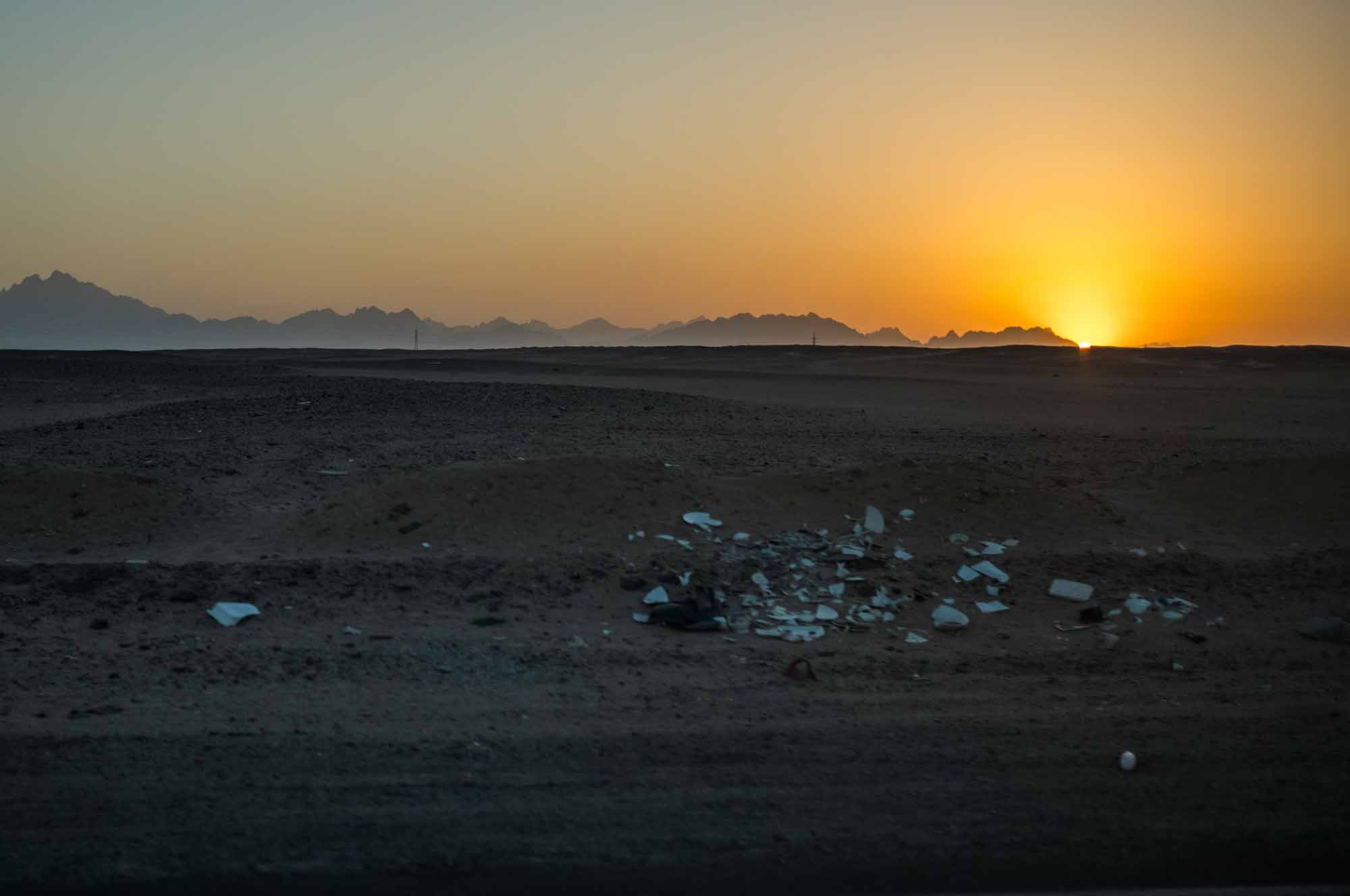 Desert landscape at sunset with distant mountains and scattered debris in the foreground.