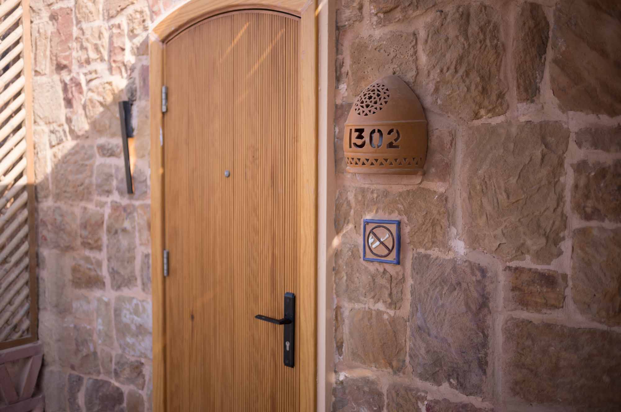 Wooden door with stone wall, room number 302 in decorative holder, no smoking sign on rustic exterior.