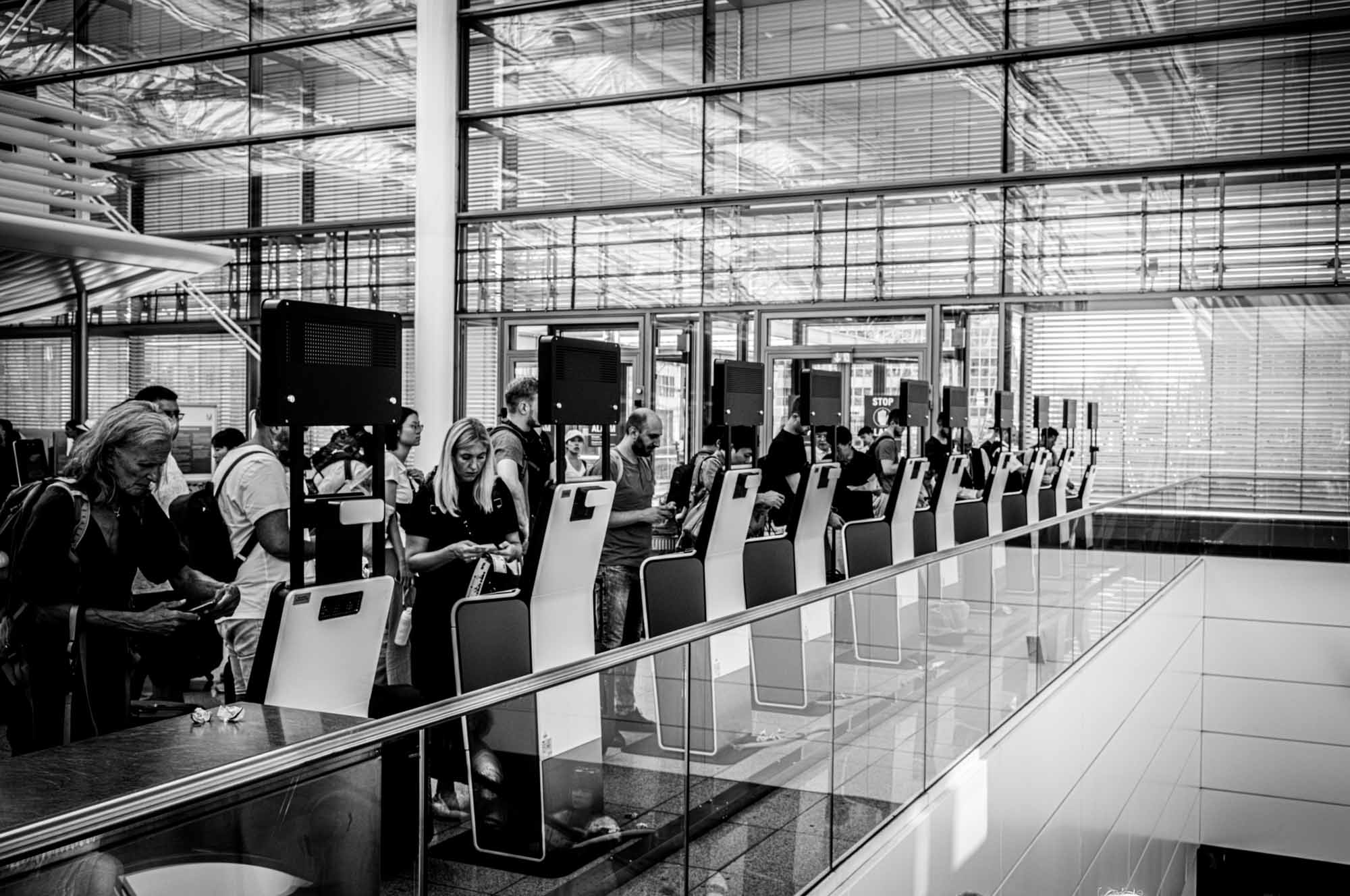 People using self-service check-in kiosks at a modern airport terminal.