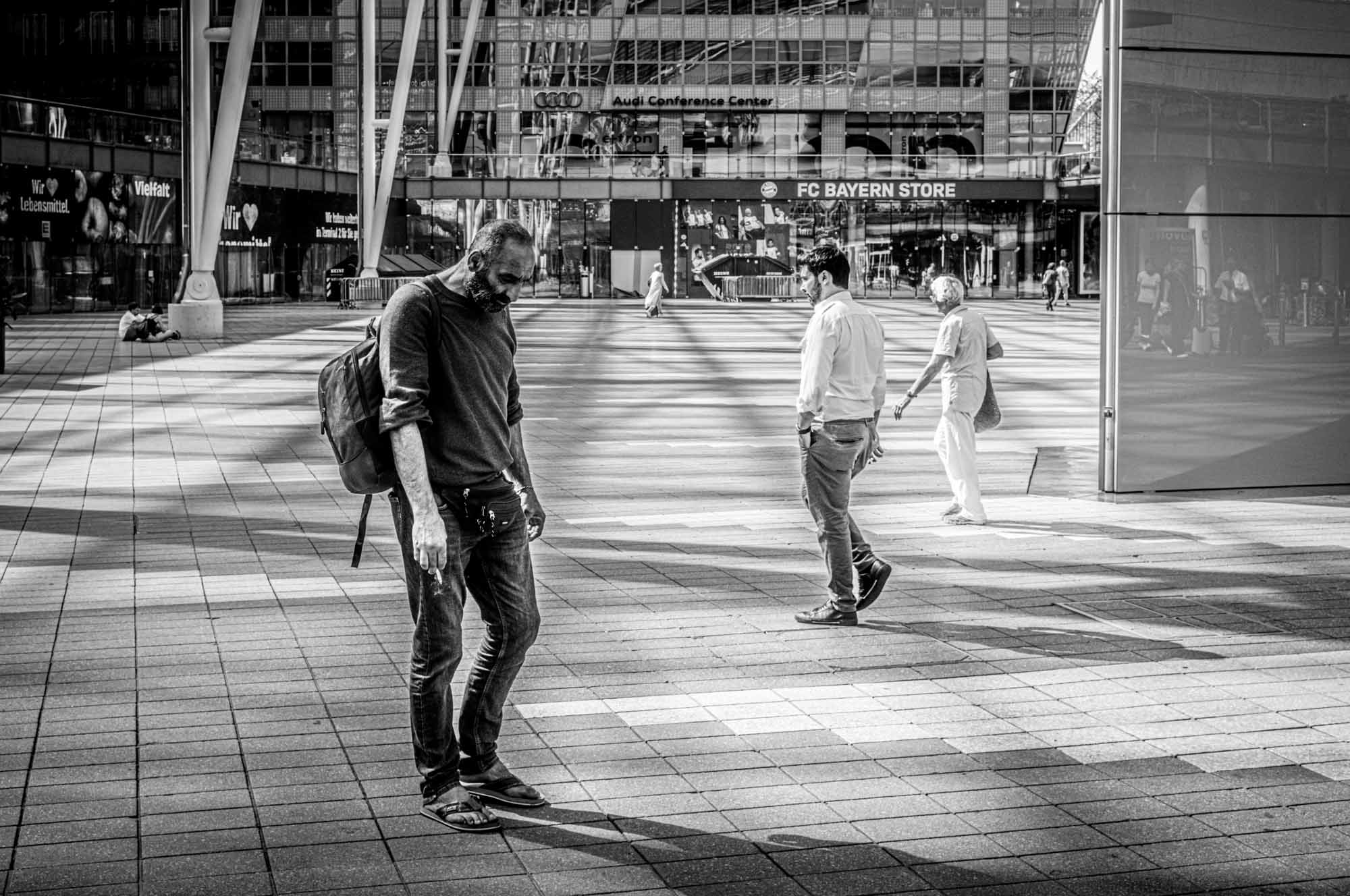 Black and white photo of people walking in front of the FC Bayern Store and Audi Conference Center.