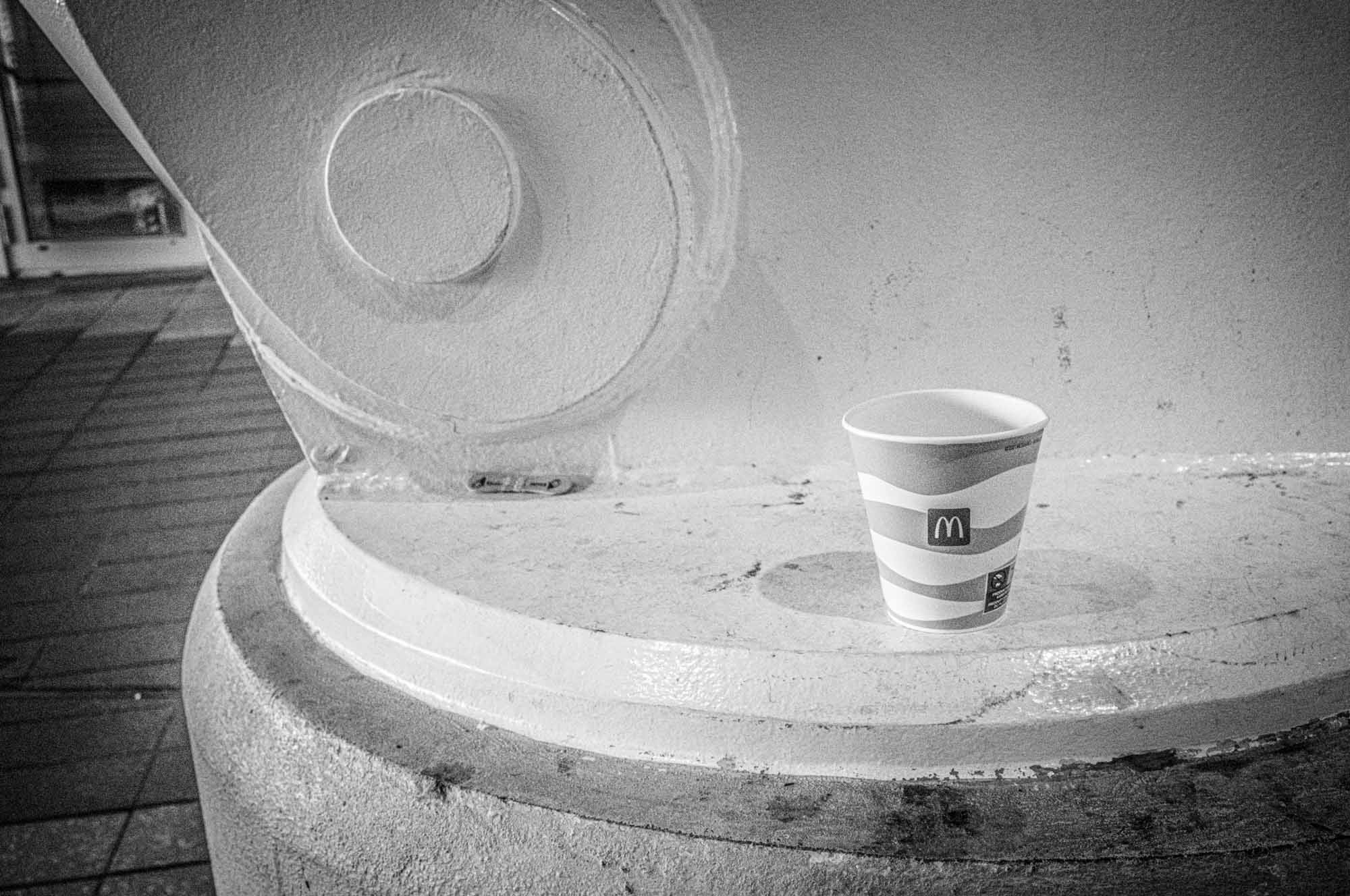 Disposable paper cup on a textured surface, grayscale photography.